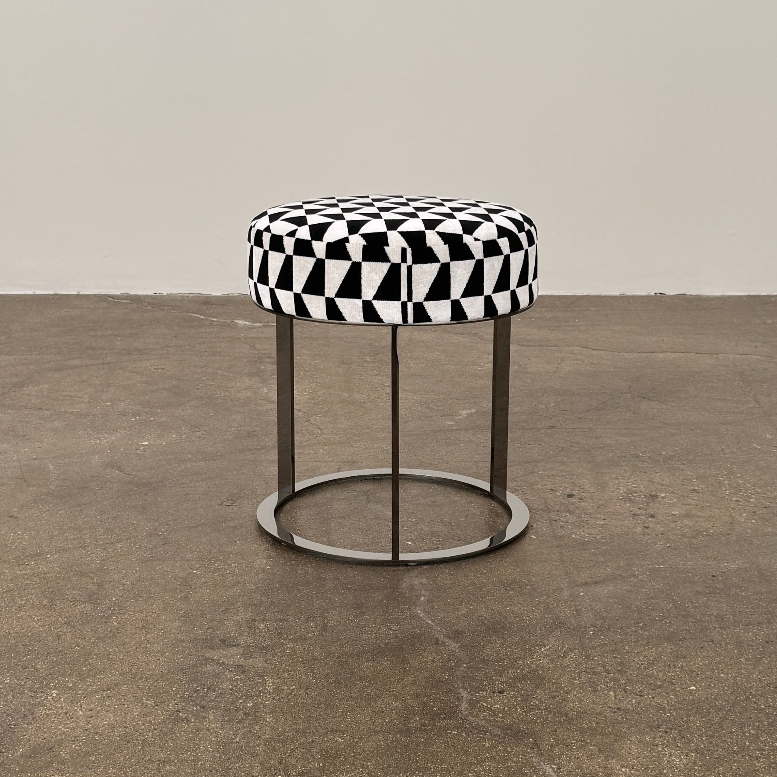 The B&B Italia Frank Ottoman features a black and white geometric cushion on a metal base with three vertical supports and a circular footrest.