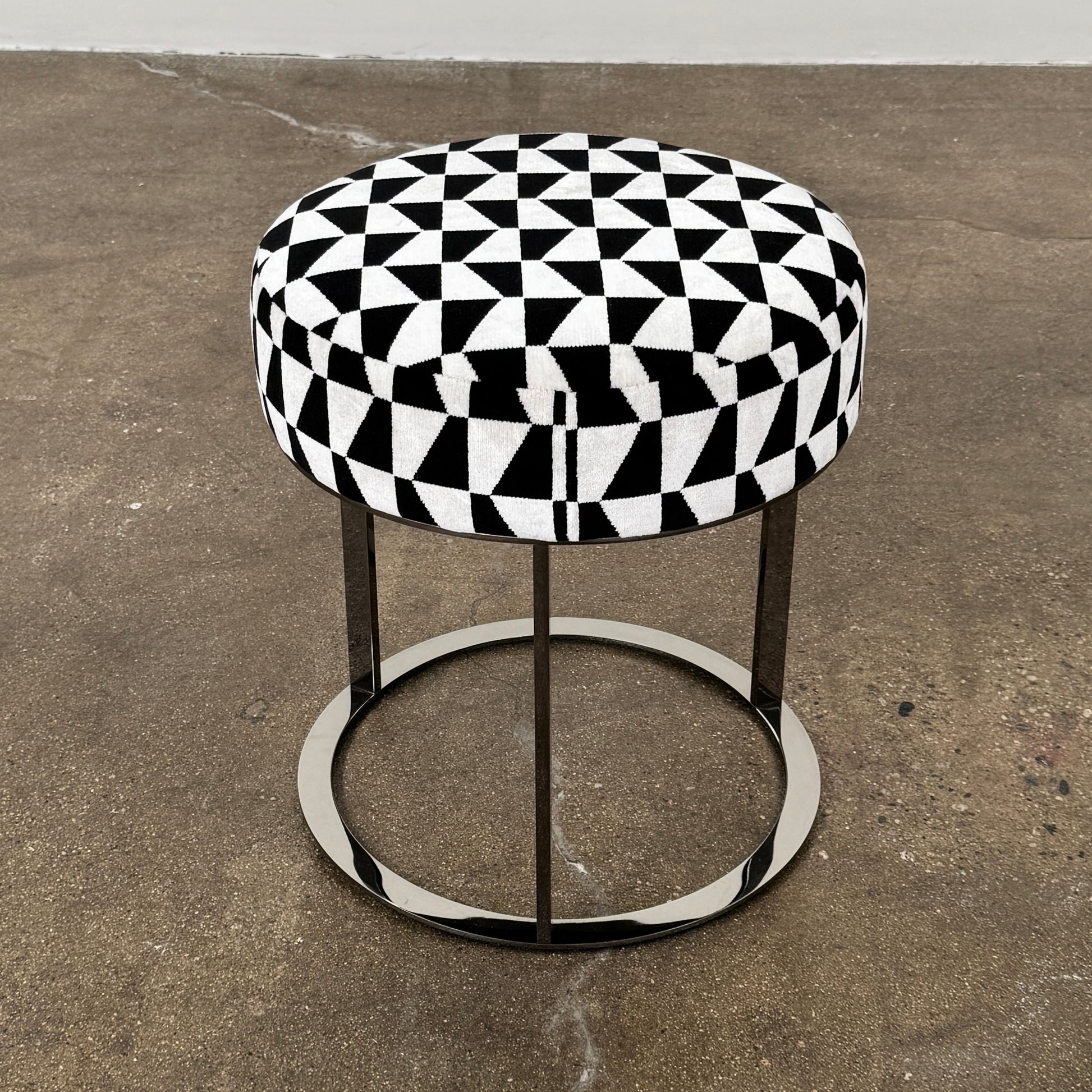 The B&B Italia Frank Ottoman features a black and white geometric cushion on a metal base with three vertical supports and a circular footrest.