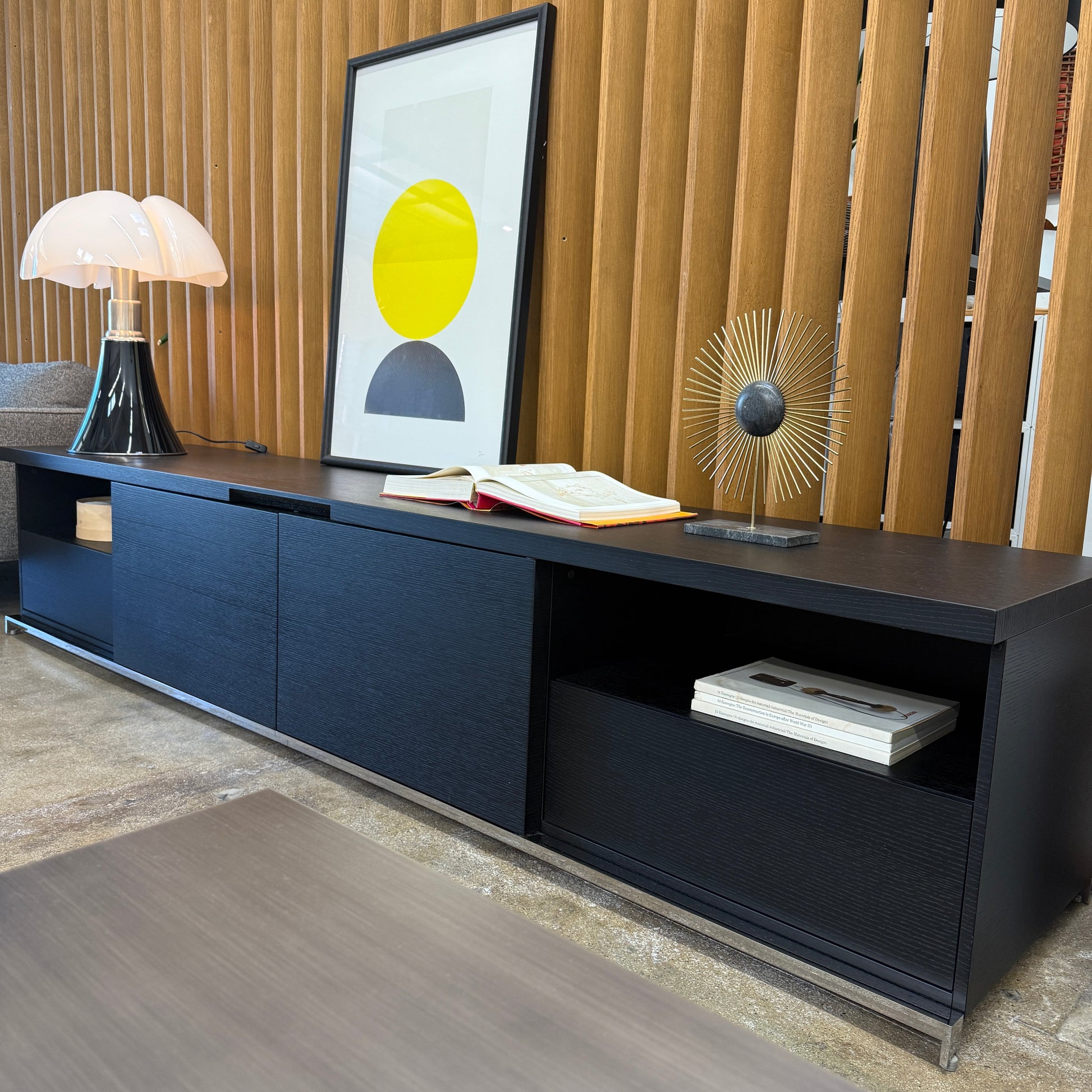 The Maxalto Mida Console by Maxalto is a modern black sideboard TV stand with three closed cabinets and two open shelves, shown on a concrete floor against a plain white background.