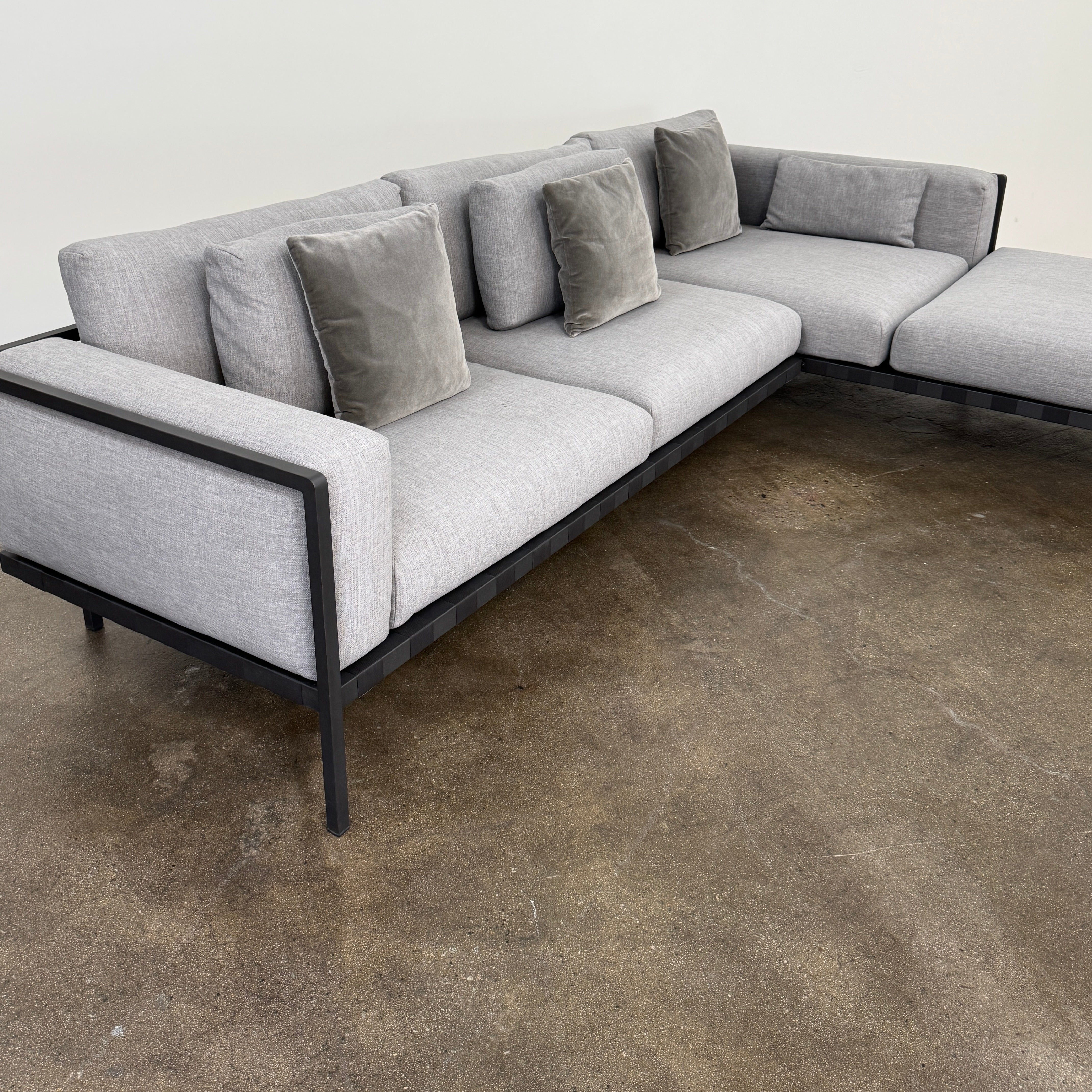The Tribu Natal Alu Outdoor Sectional Sofa by Tribú features light gray cushions, five dark gray throw pillows, and a sleek black aluminum frame—perfect for adding modern style to your patio.
