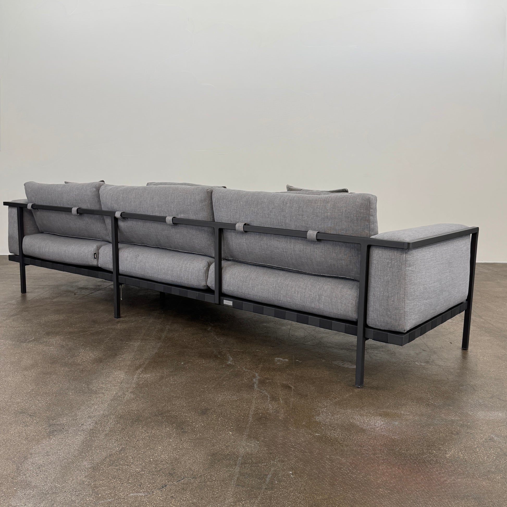 The Tribu Natal Alu Outdoor Sectional Sofa by Tribú features light gray cushions, five dark gray throw pillows, and a sleek black aluminum frame—perfect for adding modern style to your patio.