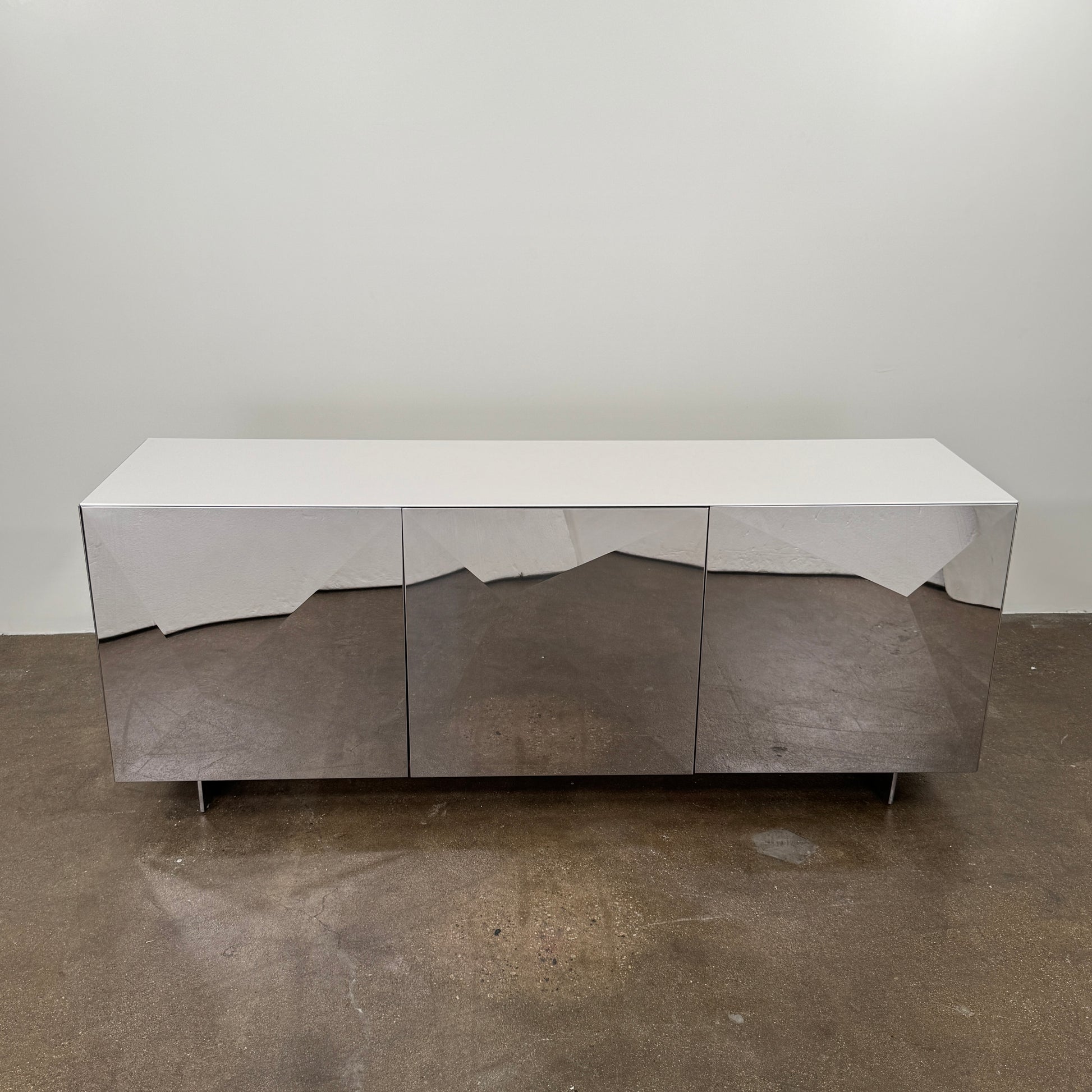 The Riflessi Cubric Sideboard by Riflessi features three mirrored doors and a geometric jagged top edge, shown here against a plain white wall on a concrete floor.