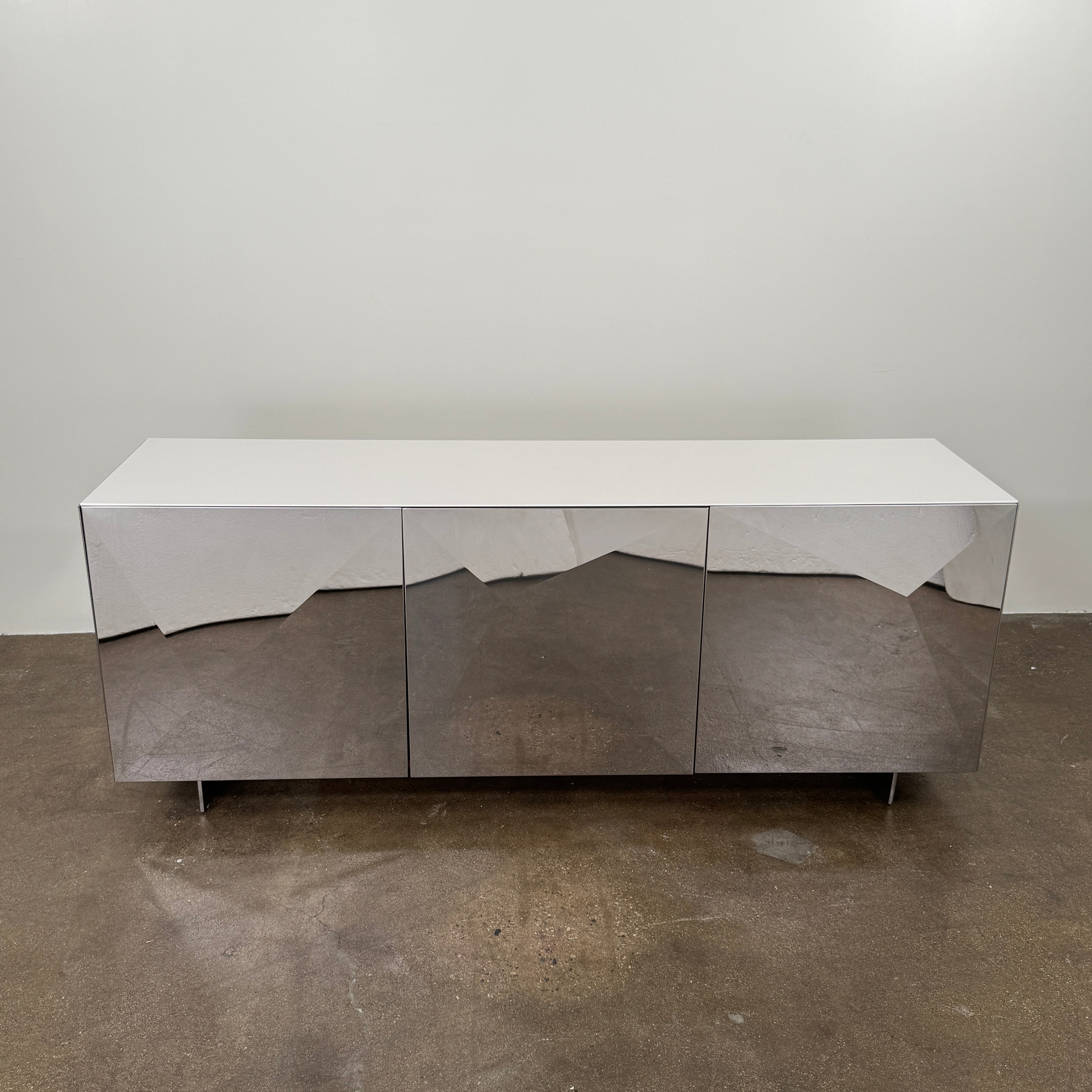 The Riflessi Cubric Sideboard by Riflessi features three mirrored doors and a geometric jagged top edge, shown here against a plain white wall on a concrete floor.