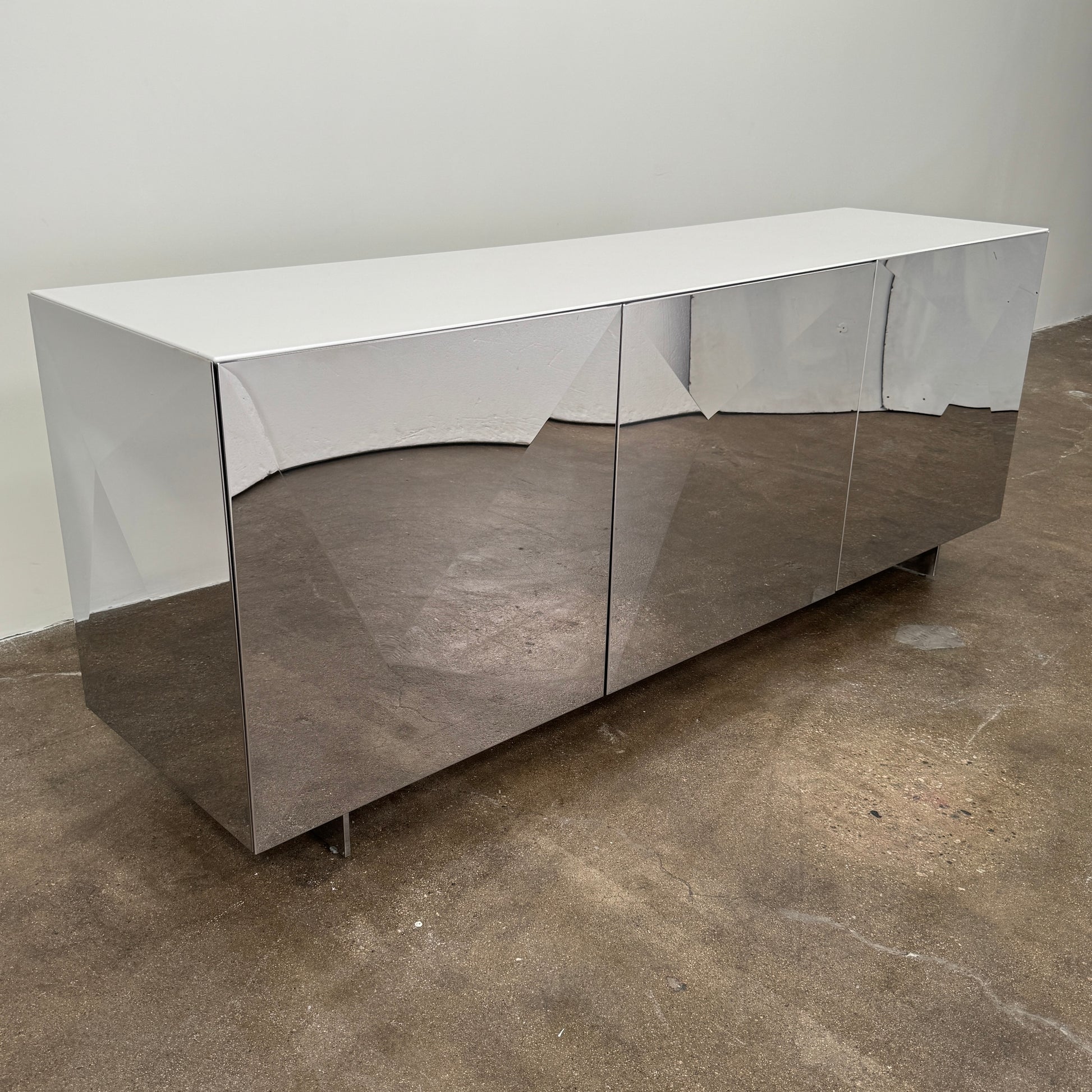 The Riflessi Cubric Sideboard by Riflessi features three mirrored doors and a geometric jagged top edge, shown here against a plain white wall on a concrete floor.