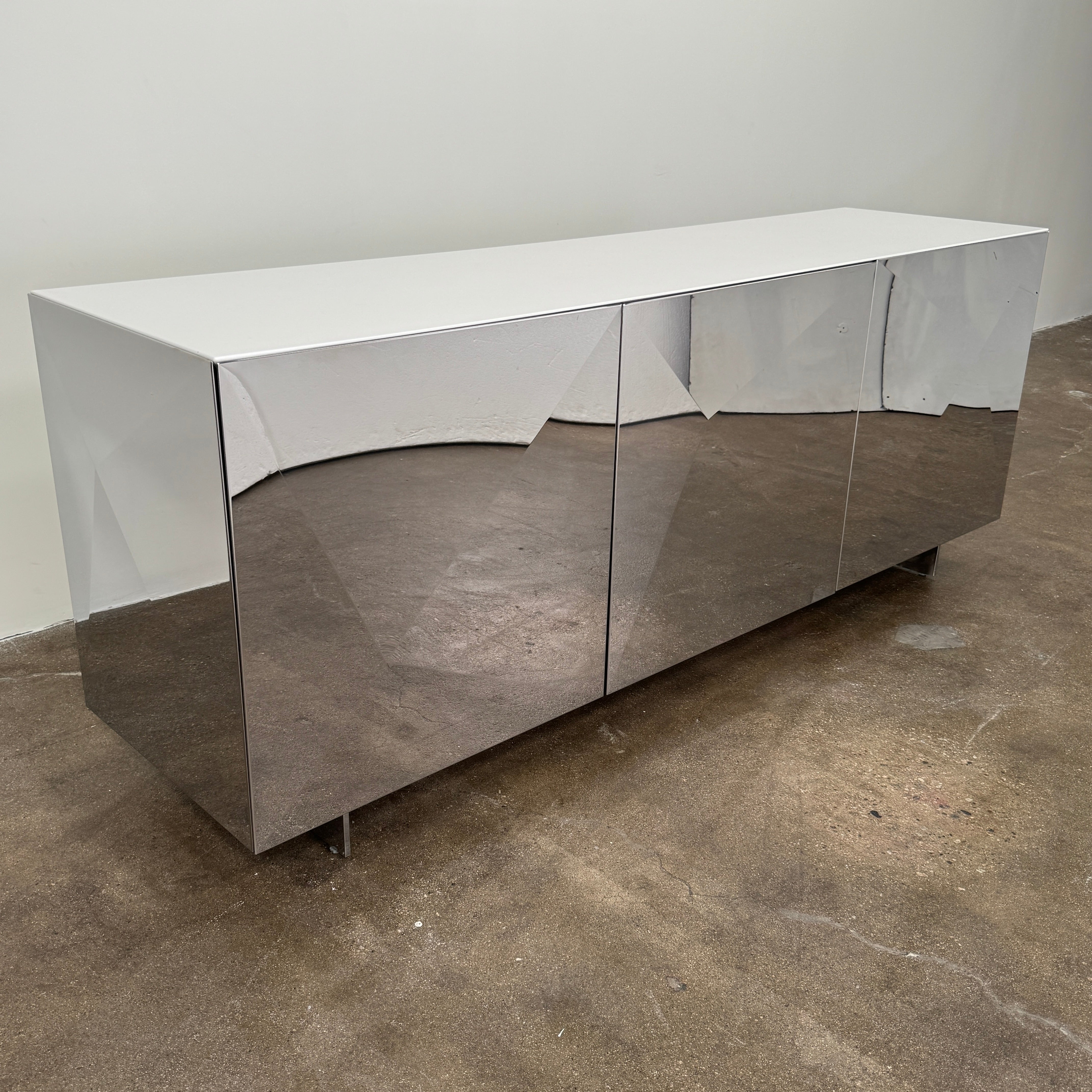 The Riflessi Cubric Sideboard by Riflessi features three mirrored doors and a geometric jagged top edge, shown here against a plain white wall on a concrete floor.