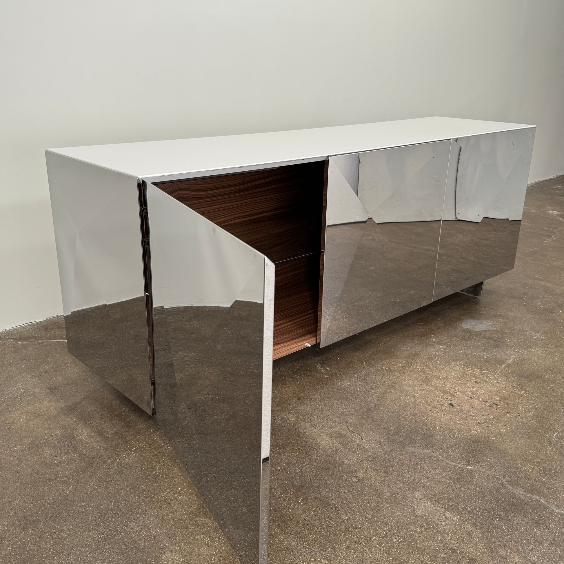 The Riflessi Cubric Sideboard by Riflessi features three mirrored doors and a geometric jagged top edge, shown here against a plain white wall on a concrete floor.