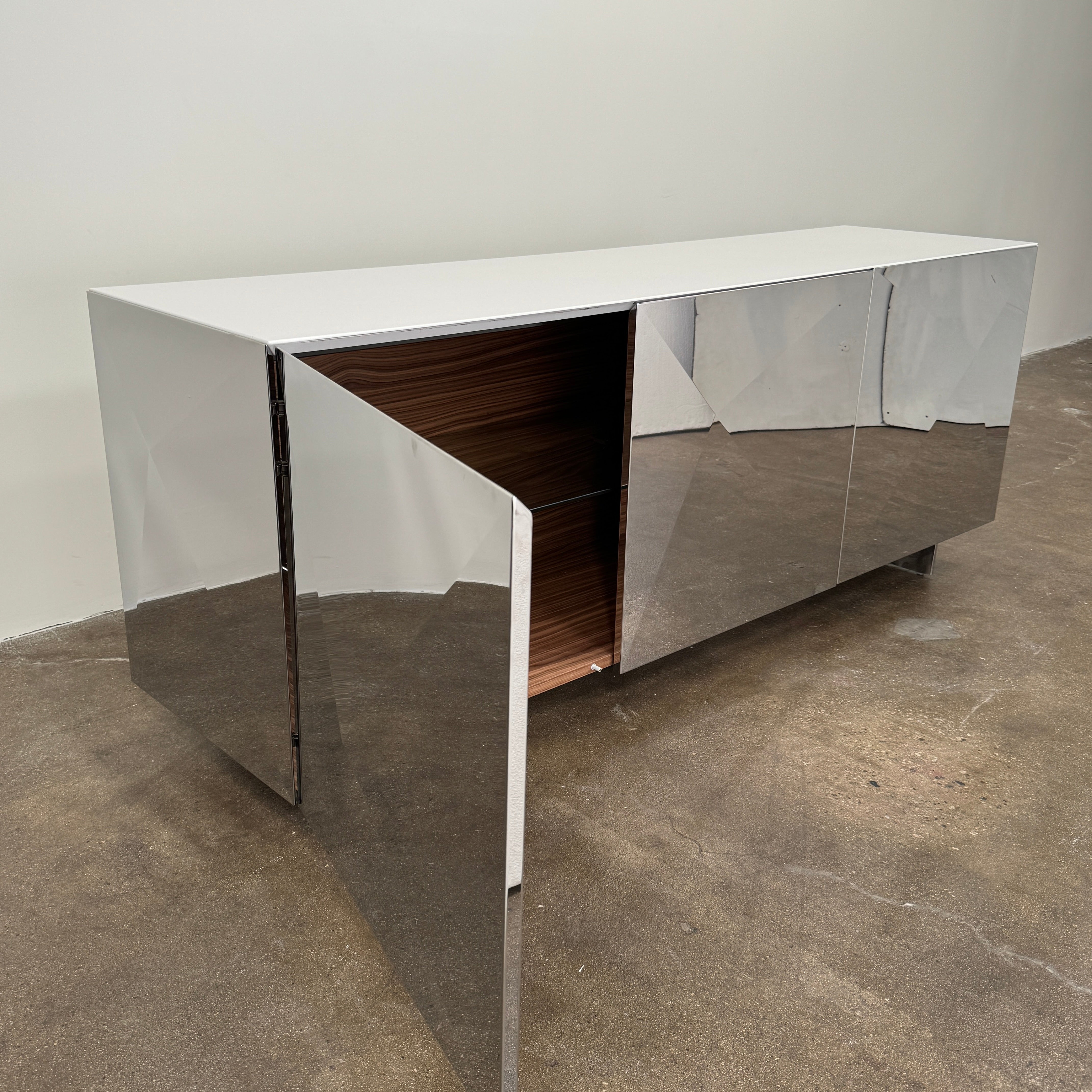The Riflessi Cubric Sideboard by Riflessi features three mirrored doors and a geometric jagged top edge, shown here against a plain white wall on a concrete floor.