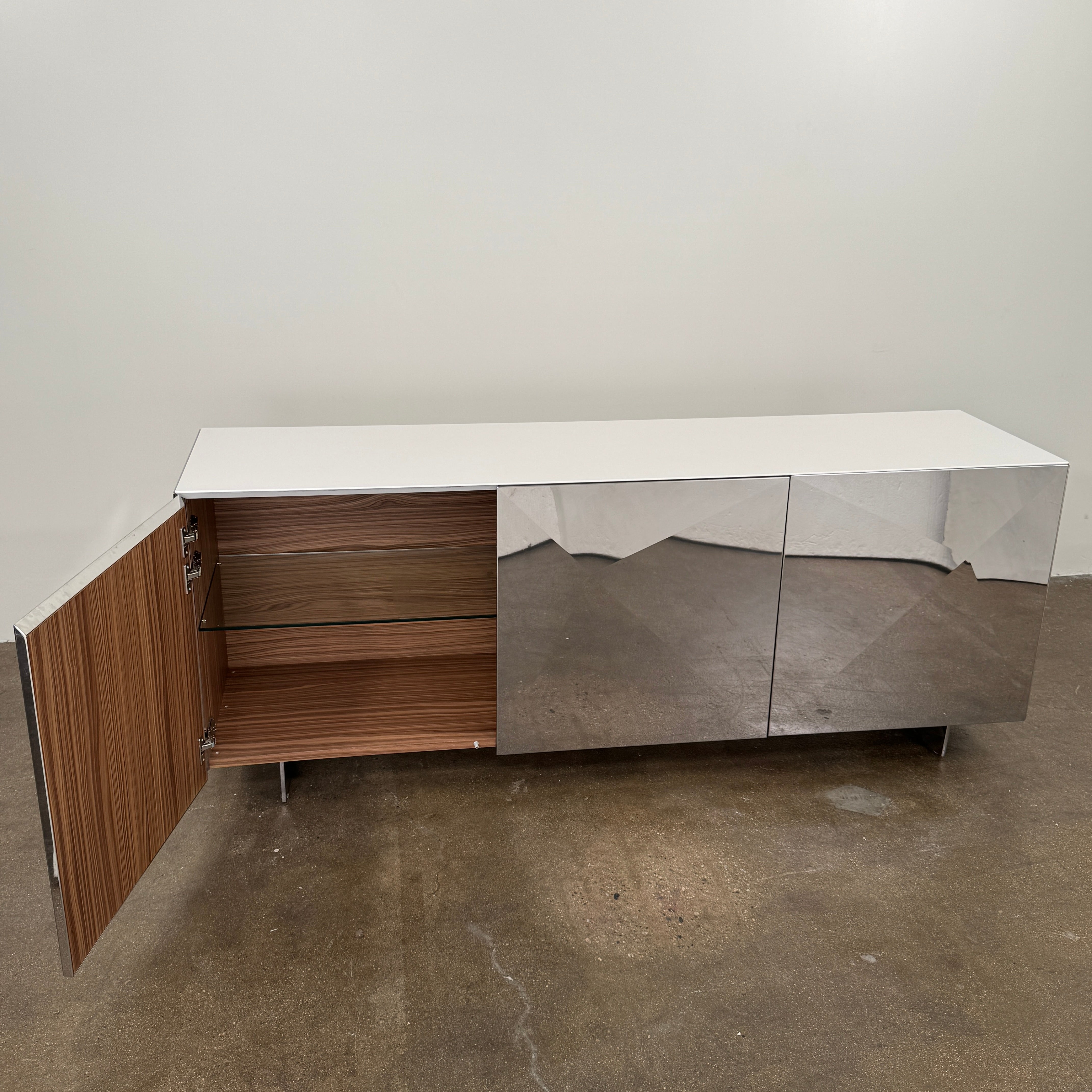 The Riflessi Cubric Sideboard by Riflessi features three mirrored doors and a geometric jagged top edge, shown here against a plain white wall on a concrete floor.