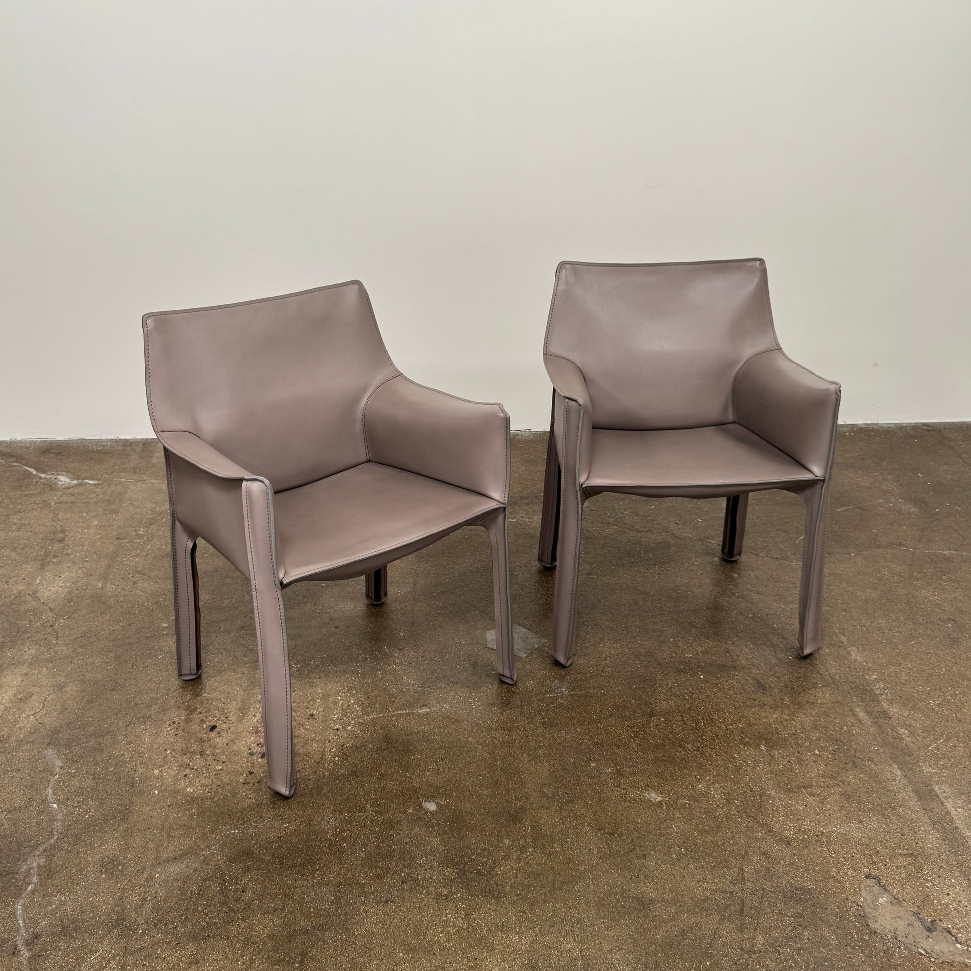 A pair of Cassina Cab 413 Dining Chairs by Modern Resale, featuring smooth taupe leather upholstery and straight legs, are placed side by side against a plain white background.