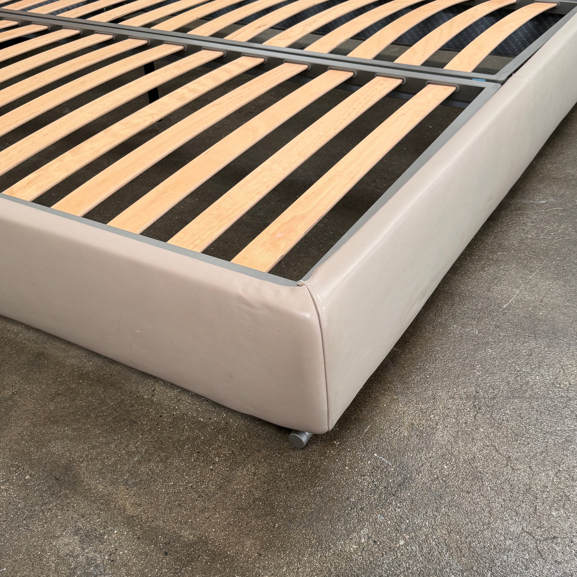 The Flexform Groundpiece Cal King Size Bed by Flexform features a beige upholstered leather frame, wide headboard, and exposed wooden slats, shown against a plain white background.