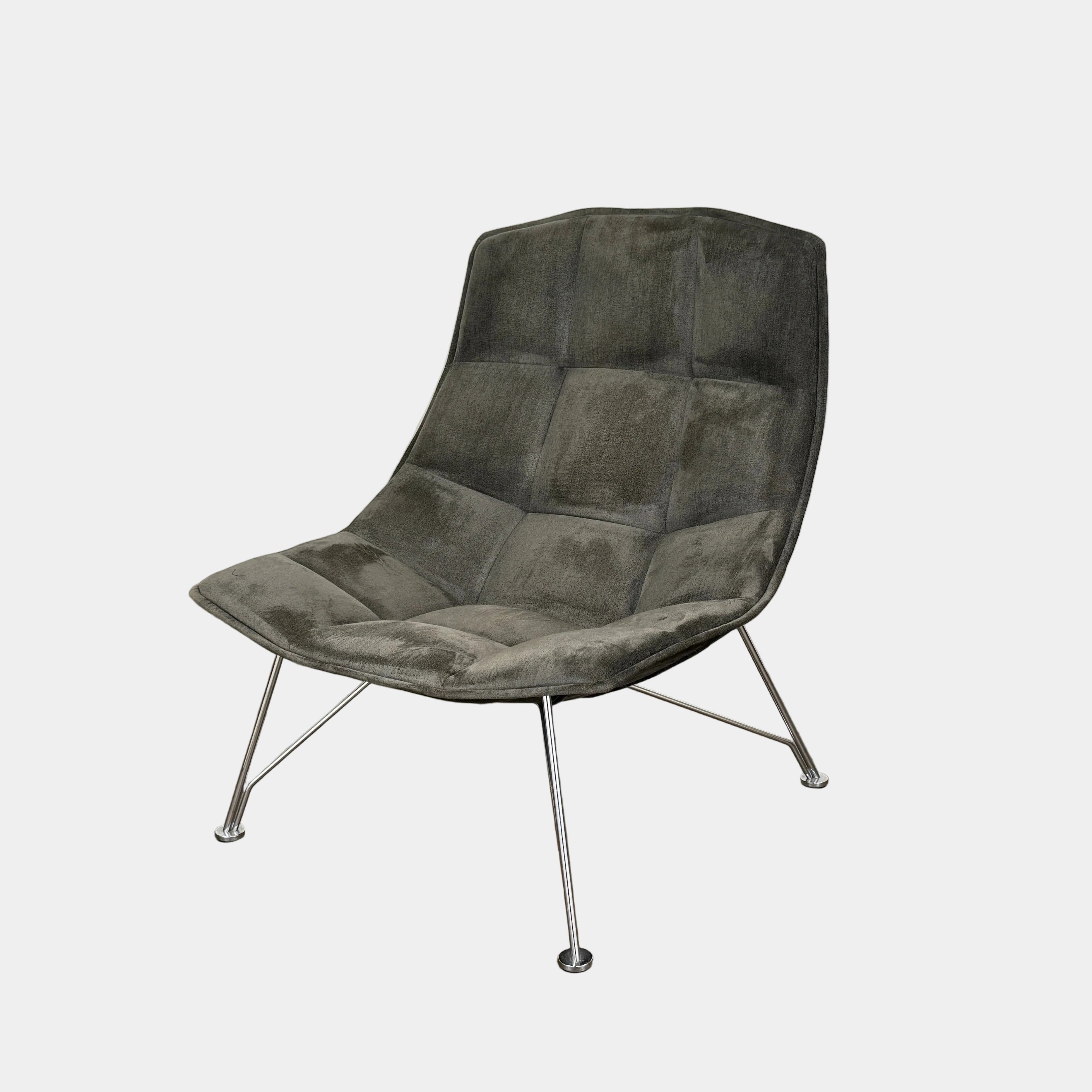 The Knoll Jehs and Laub Lounge Chair by Knoll, featuring a dark tufted fabric seat and chrome legs, is placed on a polished concrete floor against a plain white wall.
