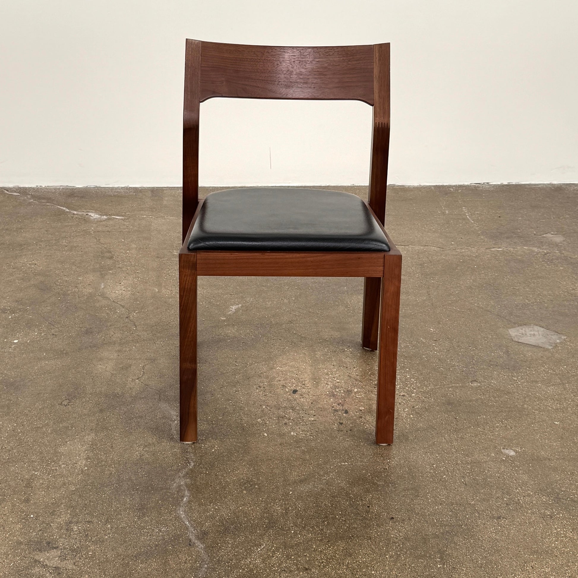 The Case Profile Dining Chair Set of 4 by Case, featuring wooden frames and black cushioned seats, is arranged on a concrete floor against a plain off-white wall.