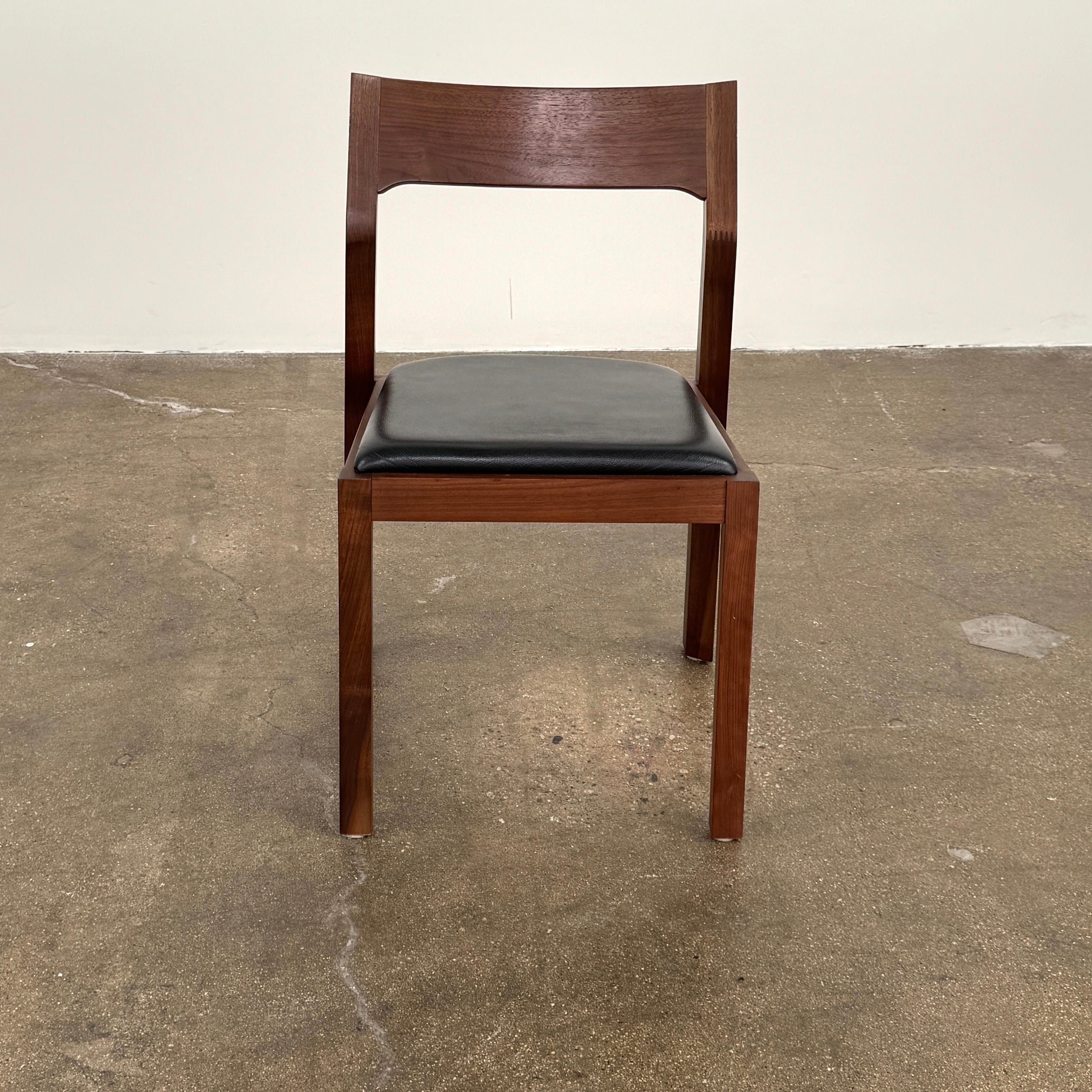 The Case Profile Dining Chair Set of 4 by Case, featuring wooden frames and black cushioned seats, is arranged on a concrete floor against a plain off-white wall.
