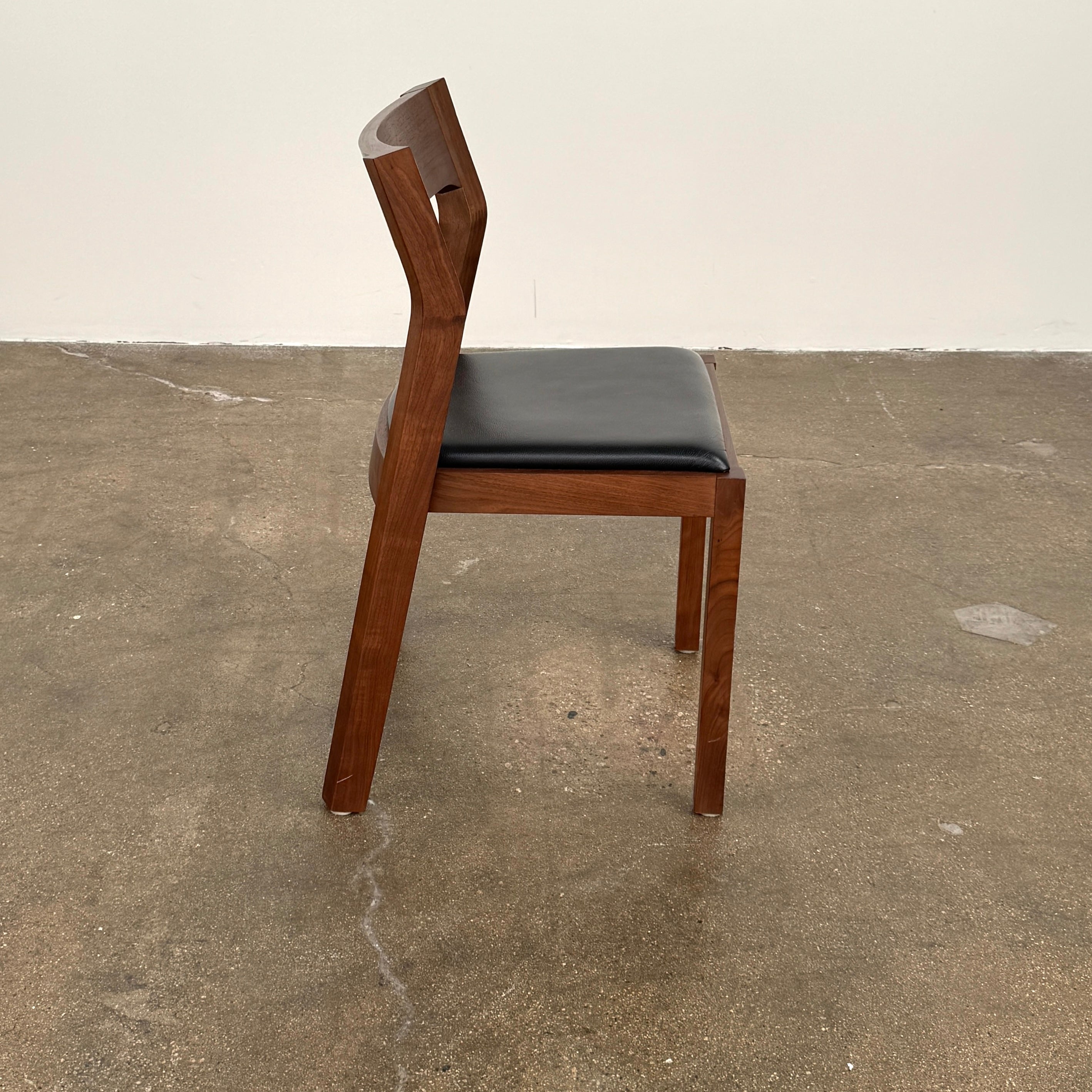The Case Profile Dining Chair Set of 4 by Case, featuring wooden frames and black cushioned seats, is arranged on a concrete floor against a plain off-white wall.