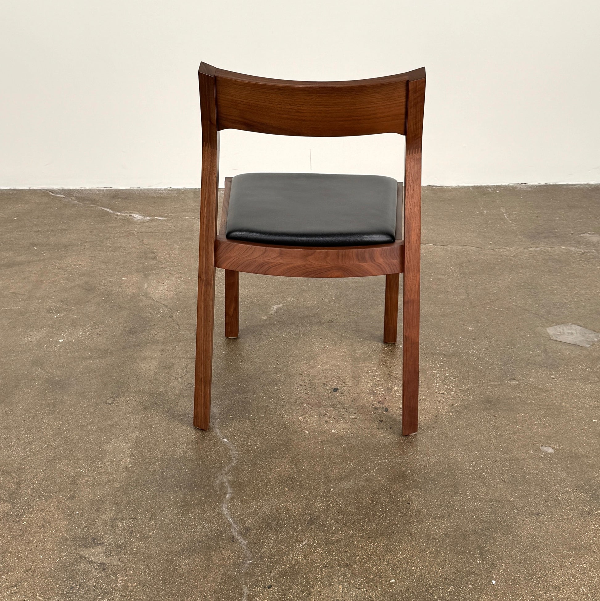 The Case Profile Dining Chair Set of 4 by Case, featuring wooden frames and black cushioned seats, is arranged on a concrete floor against a plain off-white wall.