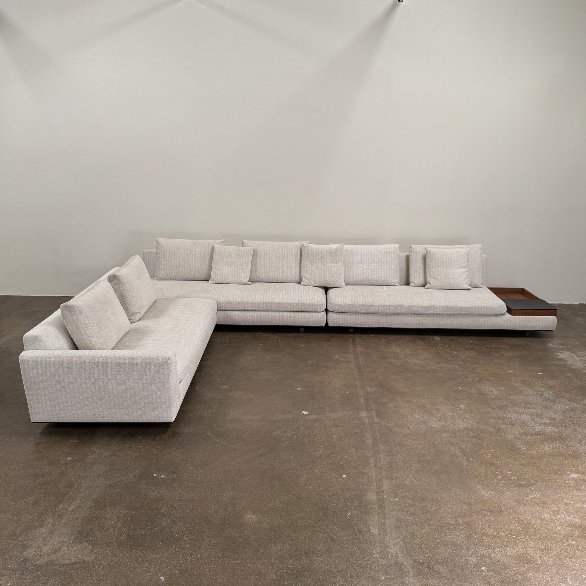 The Walter Knoll Tama Living 3 Piece Modular Sofa by Walter Knoll features an L-shaped design in light gray luxury fabric, matching cushions, and a built-in wooden side table on the right.