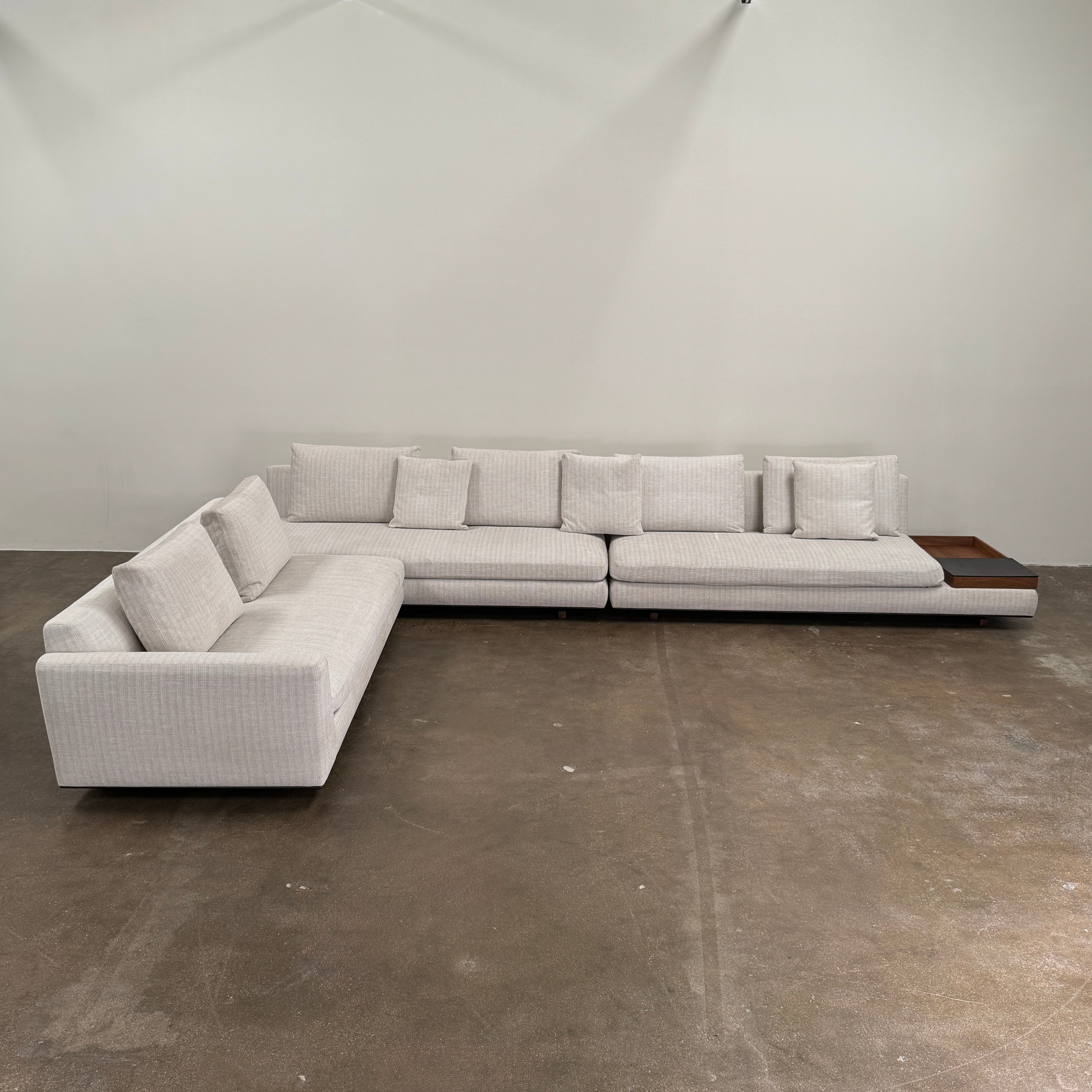 The Walter Knoll Tama Living 3 Piece Modular Sofa by Walter Knoll features an L-shaped design in light gray luxury fabric, matching cushions, and a built-in wooden side table on the right.