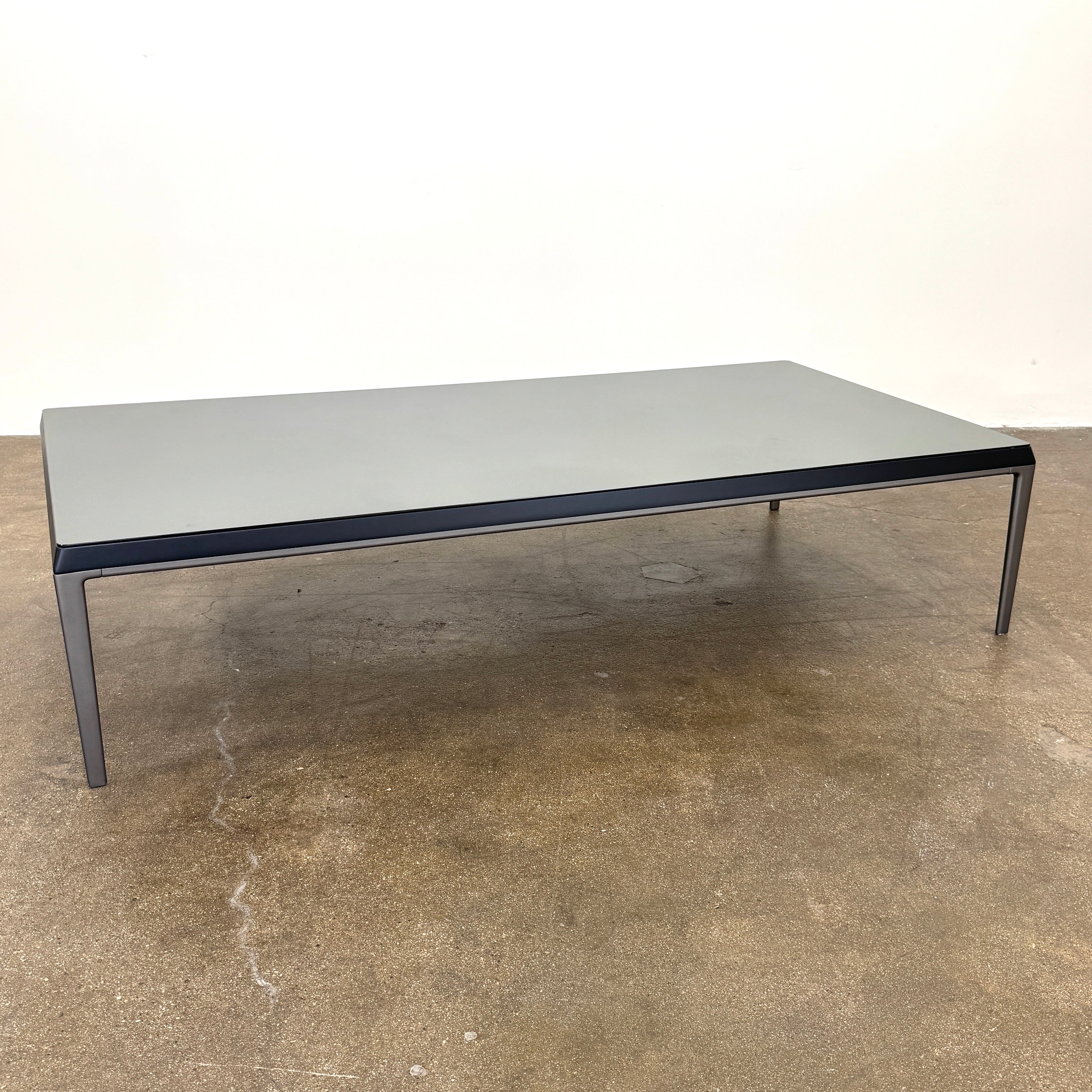 The B&B Italia Michel Coffee Table features a rectangular minimalist design with a flat gray surface and slim black metal legs, showcased against a plain white background.