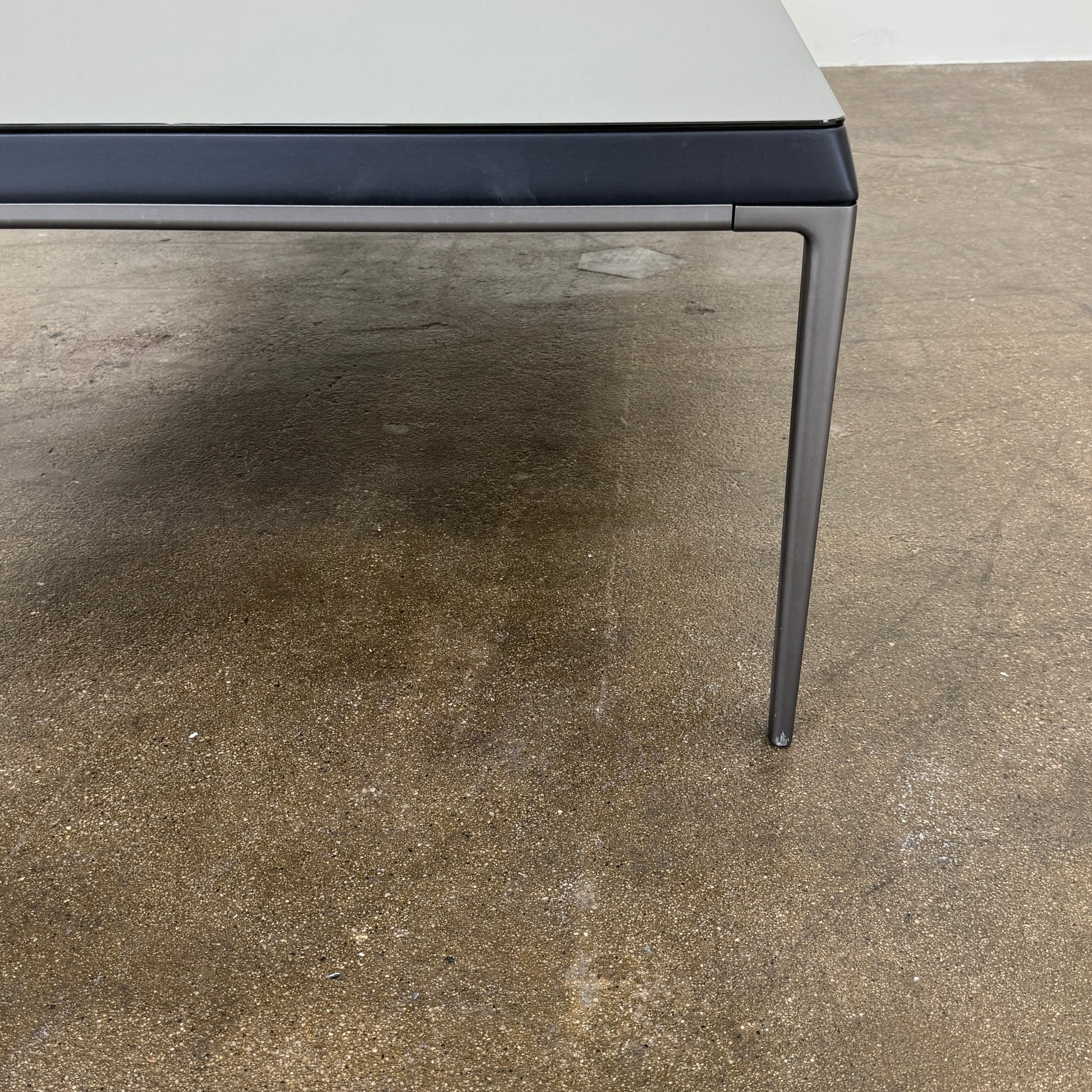 The B&B Italia Michel Coffee Table features a rectangular minimalist design with a flat gray surface and slim black metal legs, showcased against a plain white background.