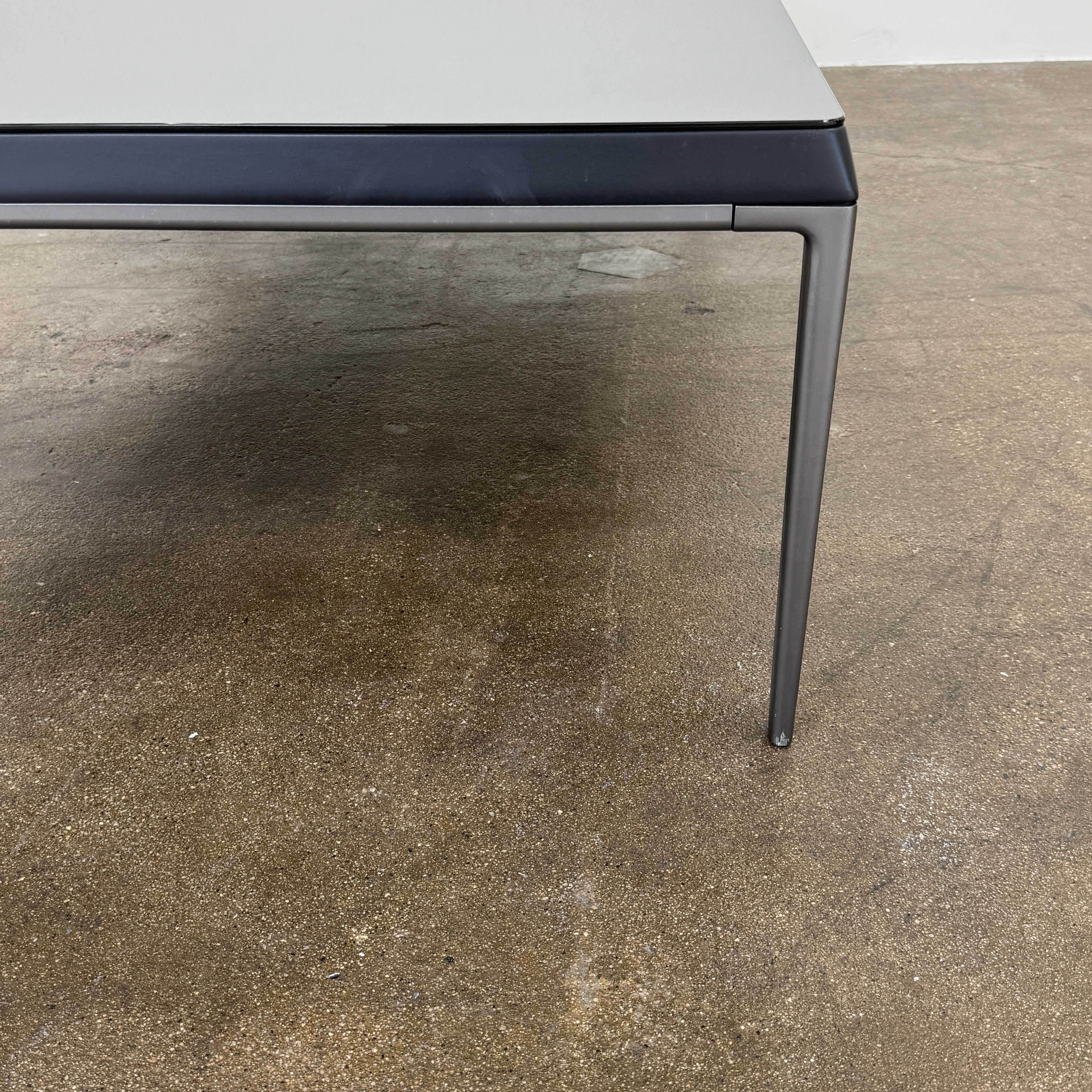 The B&B Italia Michel Coffee Table features a rectangular minimalist design with a flat gray surface and slim black metal legs, showcased against a plain white background.