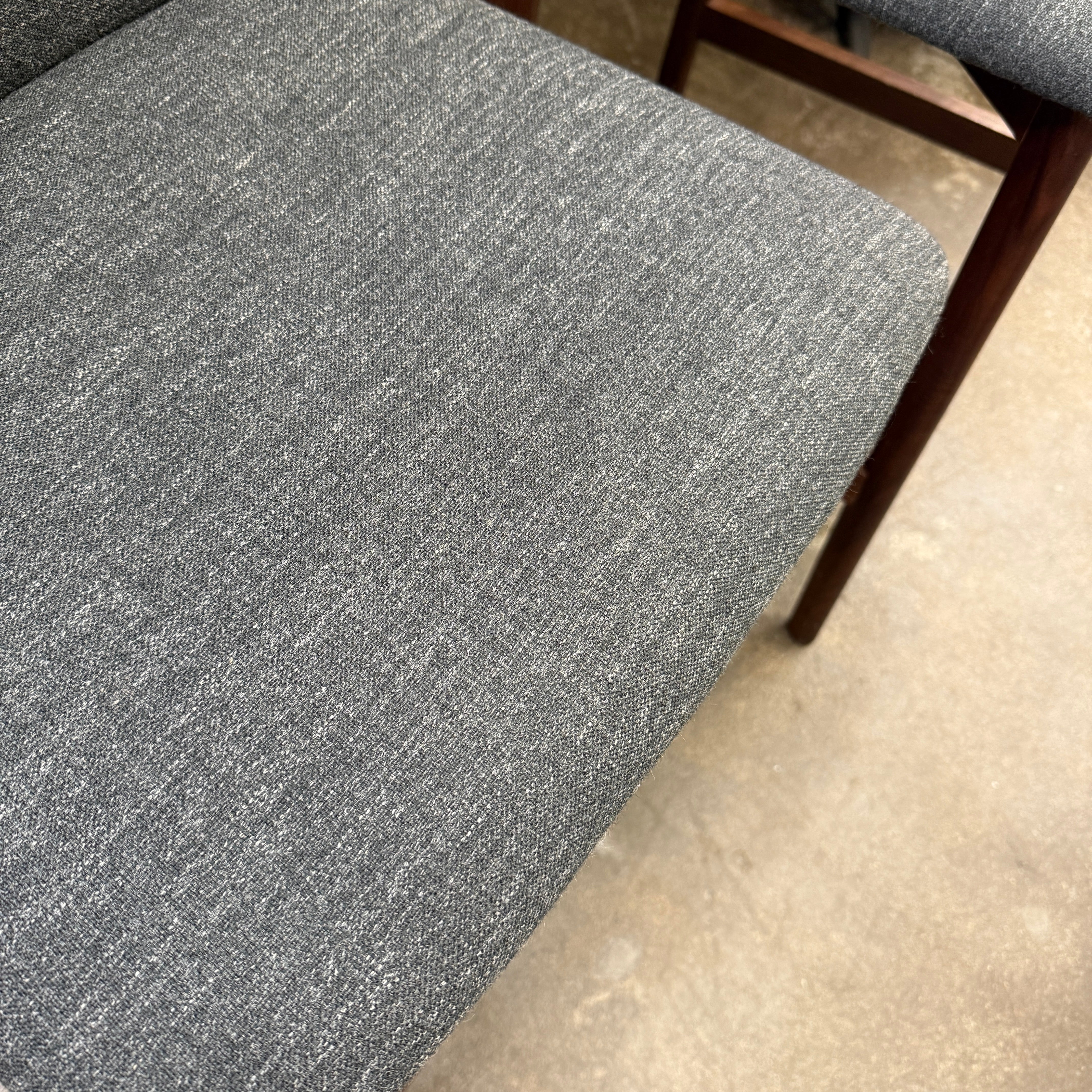 Three DWR Contour Counter Stools (Set of 3) with dark grey upholstered seats and walnut frames are arranged in a row on a polished concrete floor against a plain white wall.