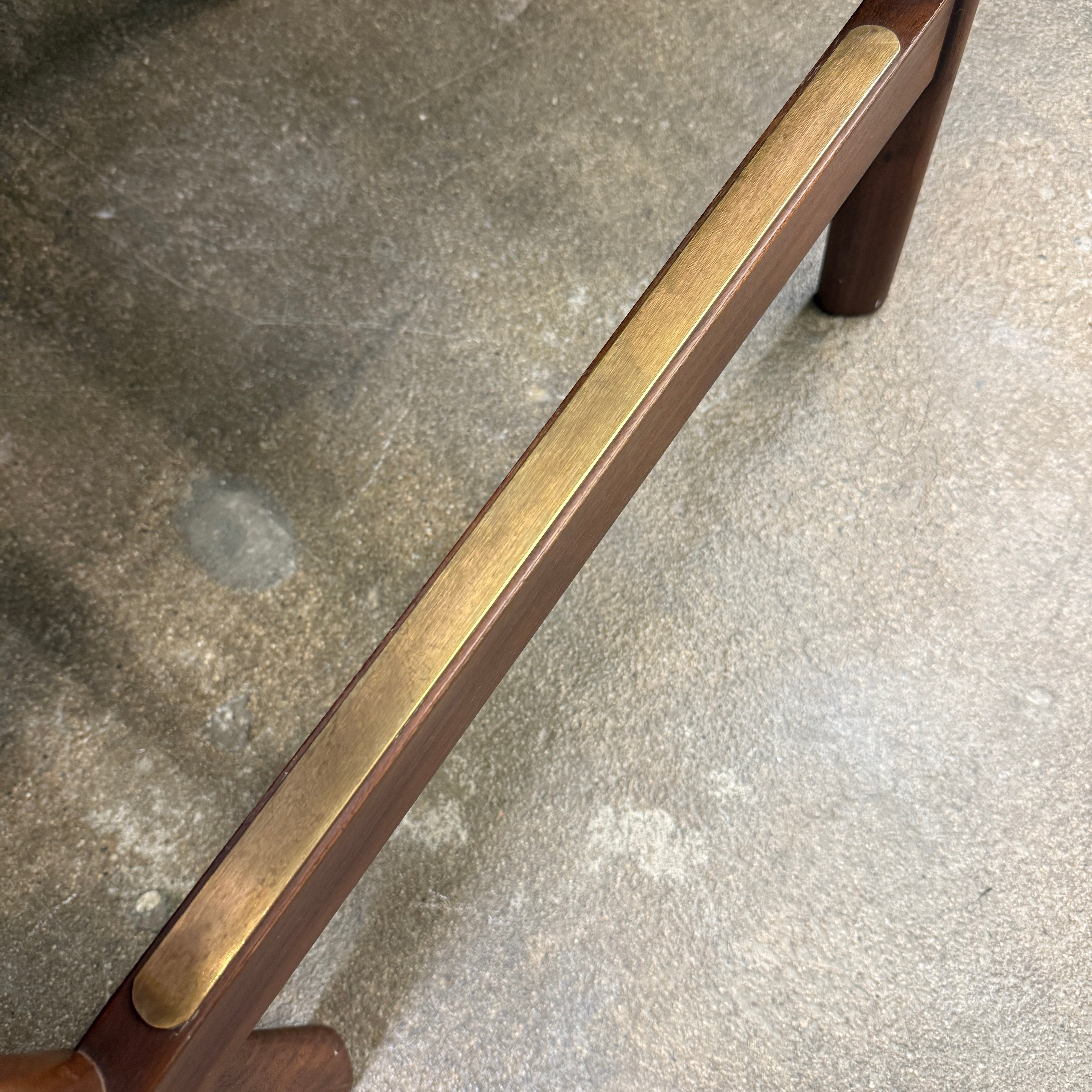 Three DWR Contour Counter Stools (Set of 3) with dark grey upholstered seats and walnut frames are arranged in a row on a polished concrete floor against a plain white wall.