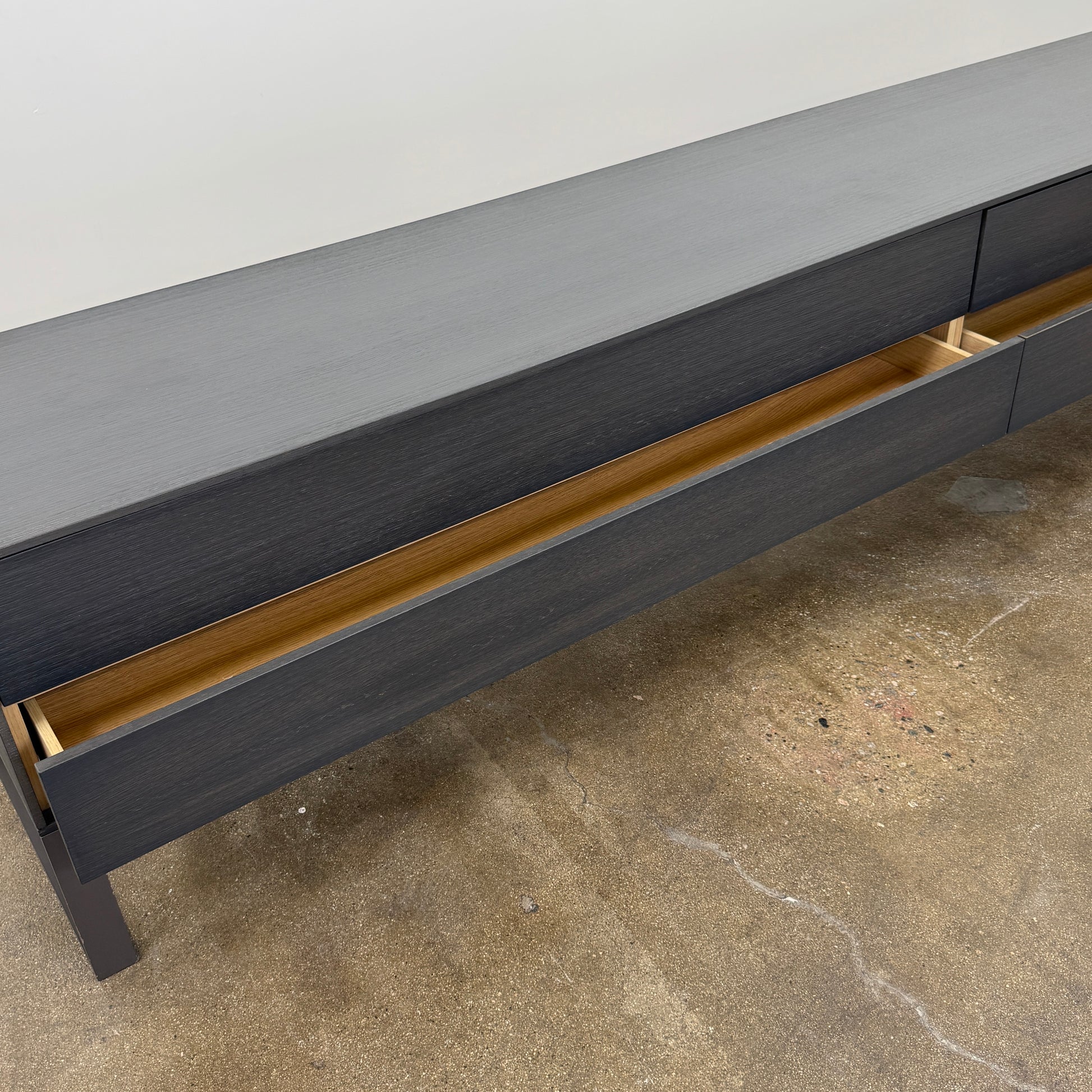 The Joan Lao Custom Media Console by Joan Lao is a black, modern low-profile piece made from sustainably sourced wood, featuring four drawers and open rectangular legs, shown against a plain white background.