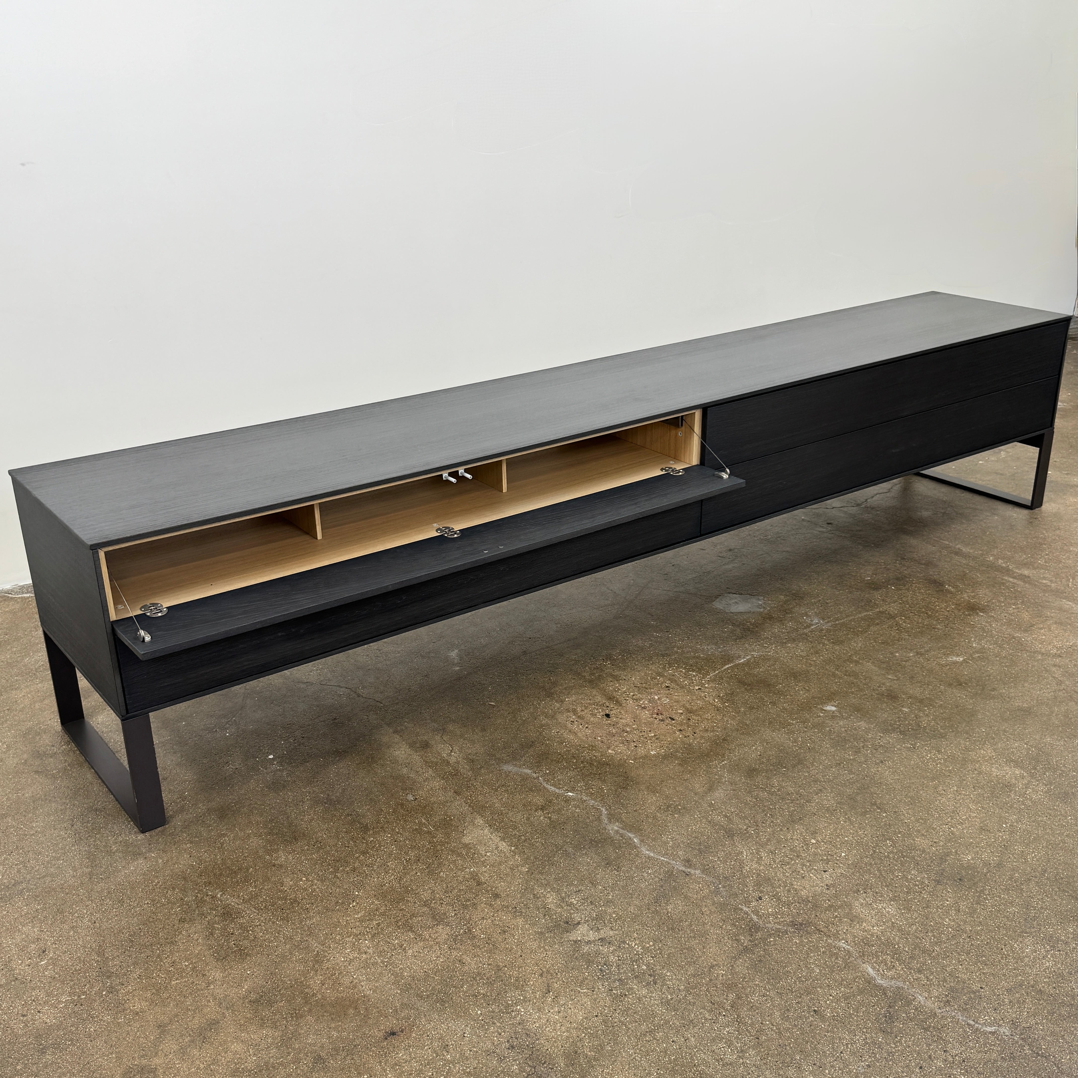 The Joan Lao Custom Media Console by Joan Lao is a black, modern low-profile piece made from sustainably sourced wood, featuring four drawers and open rectangular legs, shown against a plain white background.