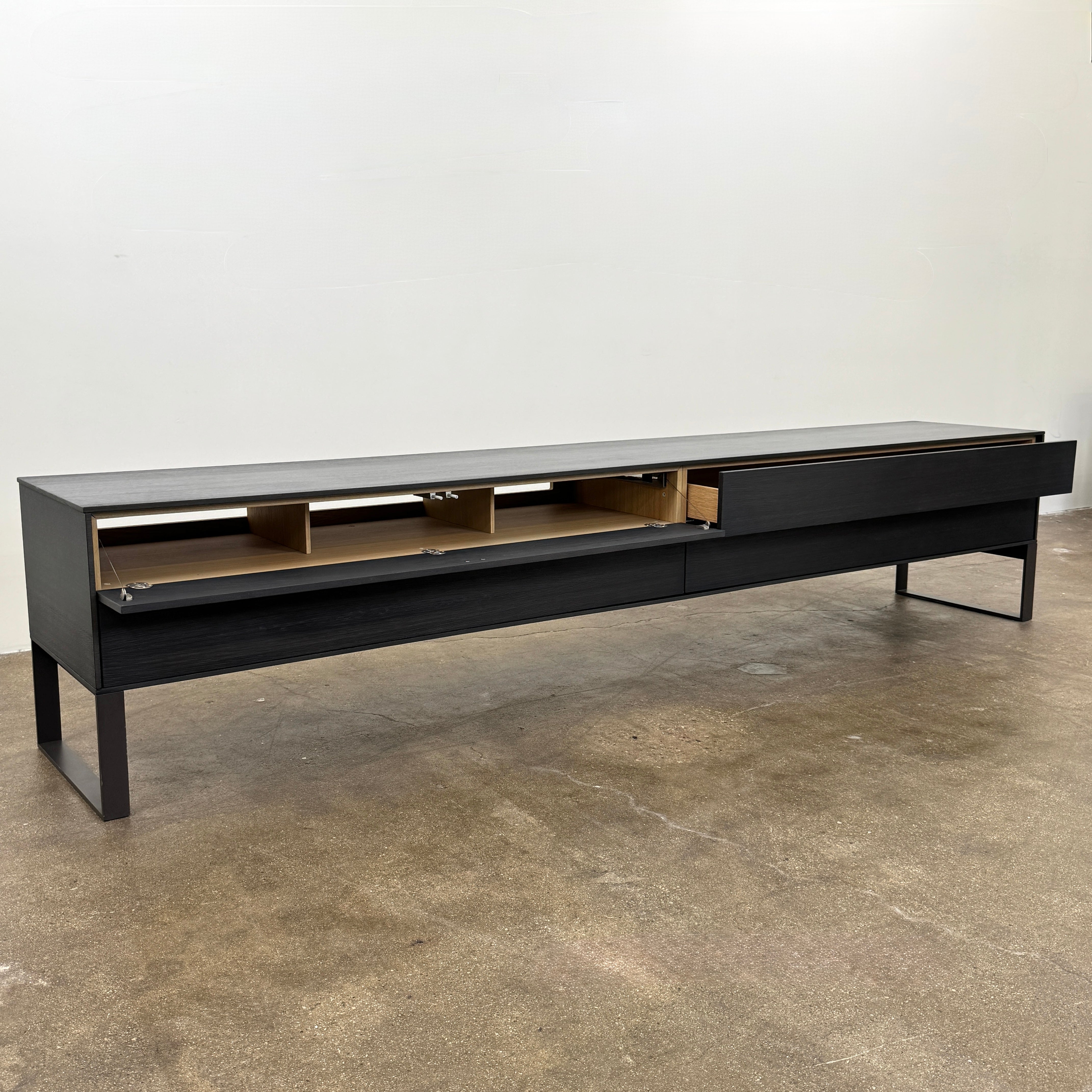 The Joan Lao Custom Media Console by Joan Lao is a black, modern low-profile piece made from sustainably sourced wood, featuring four drawers and open rectangular legs, shown against a plain white background.