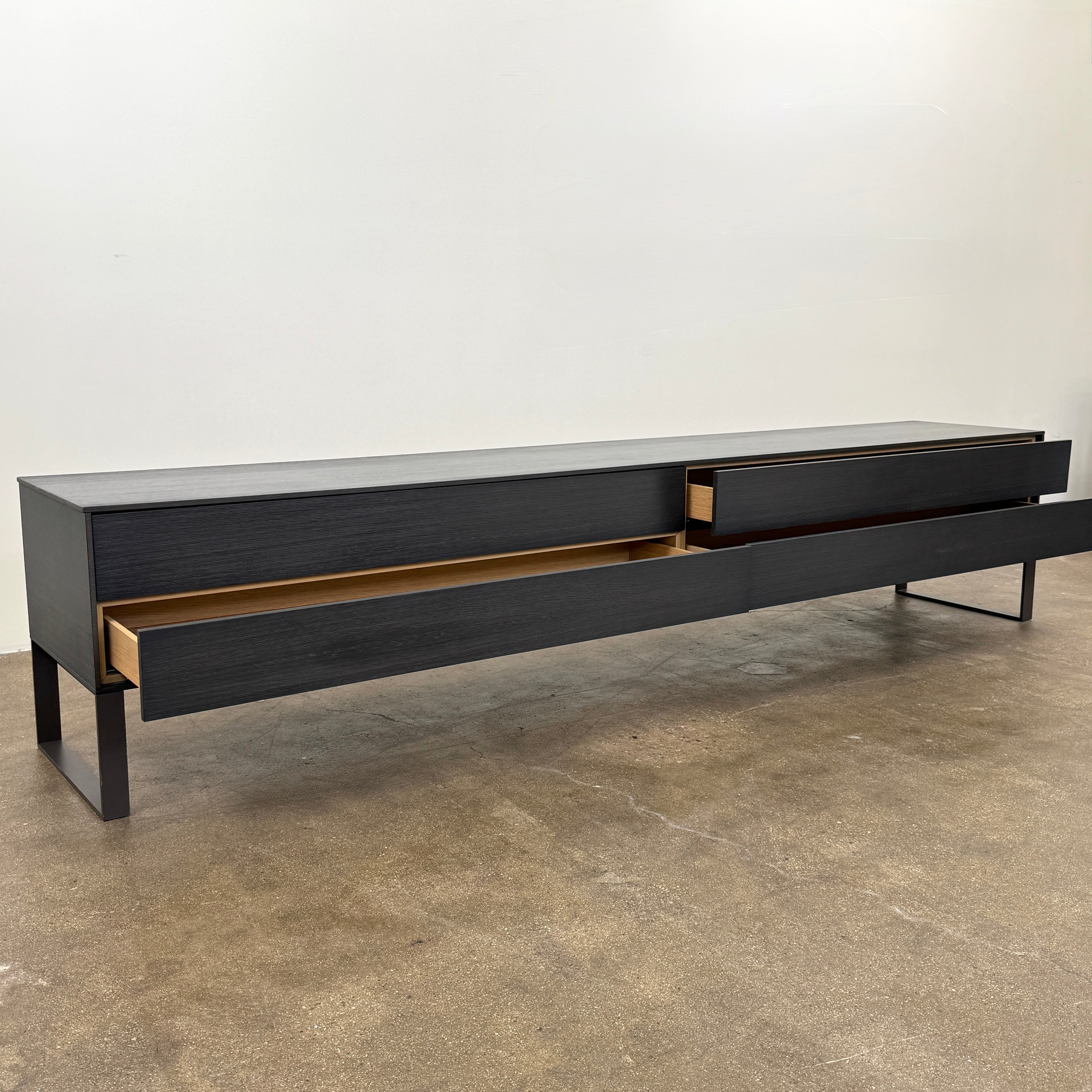 The Joan Lao Custom Media Console by Joan Lao is a black, modern low-profile piece made from sustainably sourced wood, featuring four drawers and open rectangular legs, shown against a plain white background.