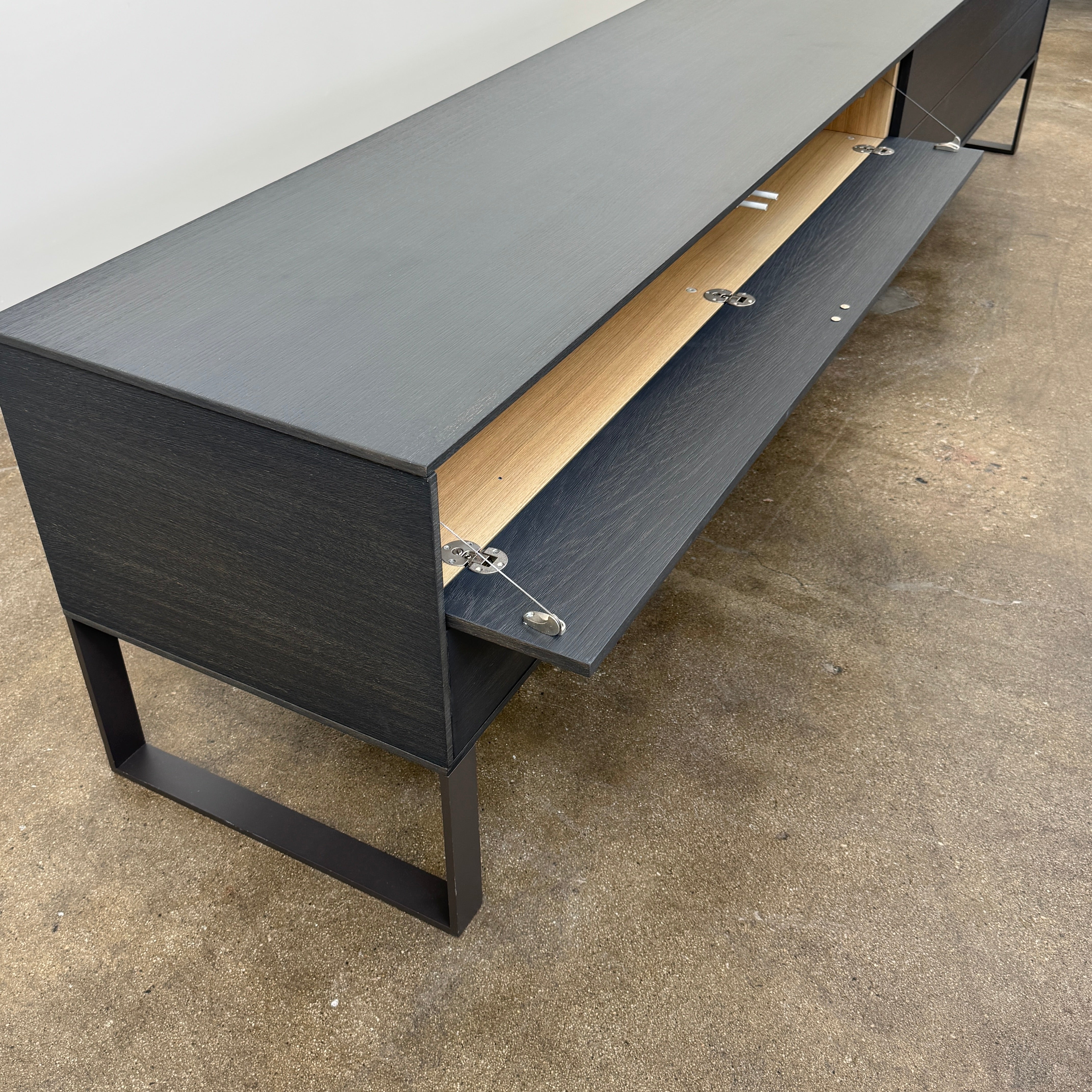 The Joan Lao Custom Media Console by Joan Lao is a black, modern low-profile piece made from sustainably sourced wood, featuring four drawers and open rectangular legs, shown against a plain white background.