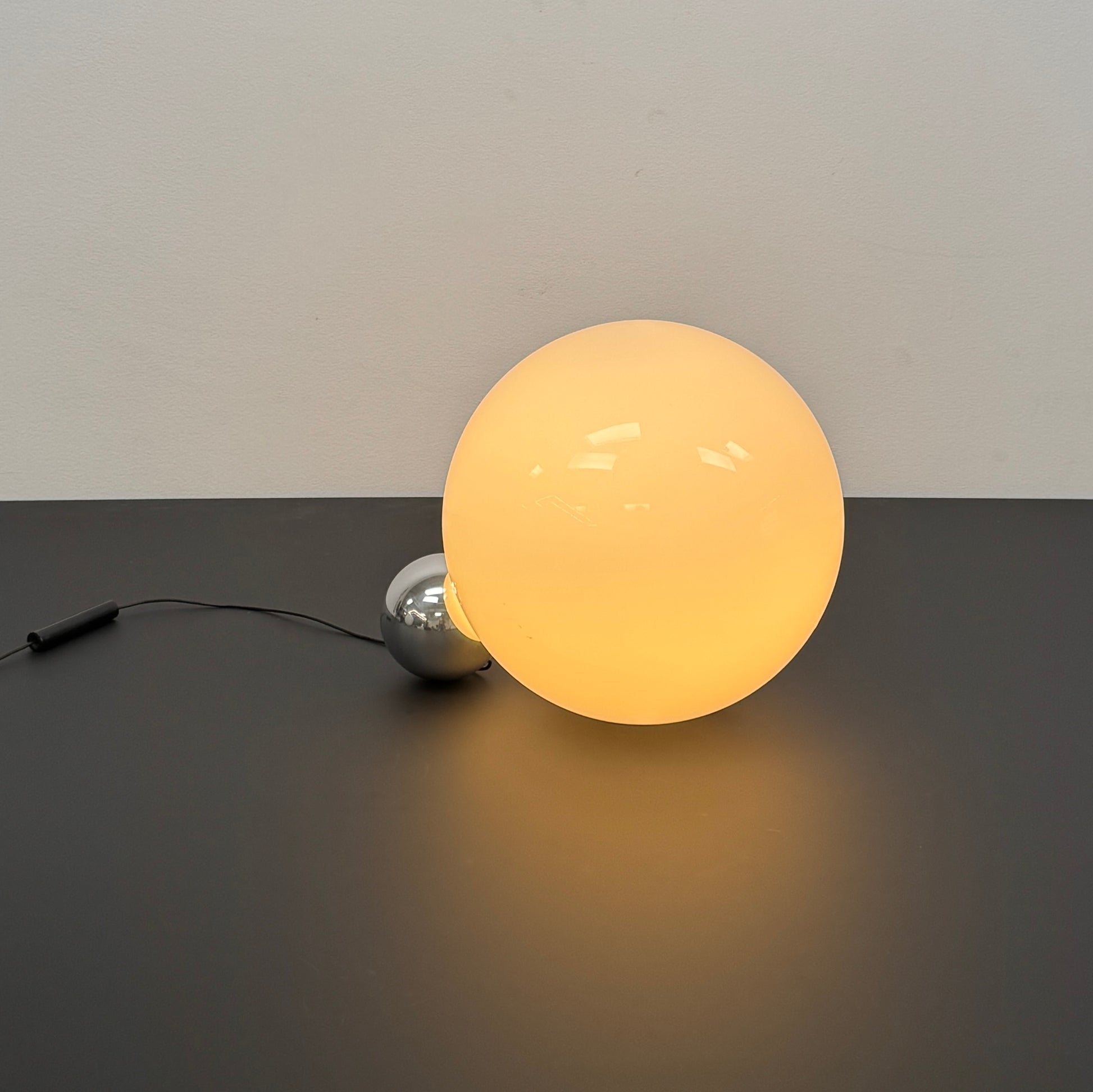 Two Flos Copycat Table Lamps by Flos, featuring glowing frosted glass spheres and chrome bases, make a sculptural statement on a dark surface against a light-colored wall.