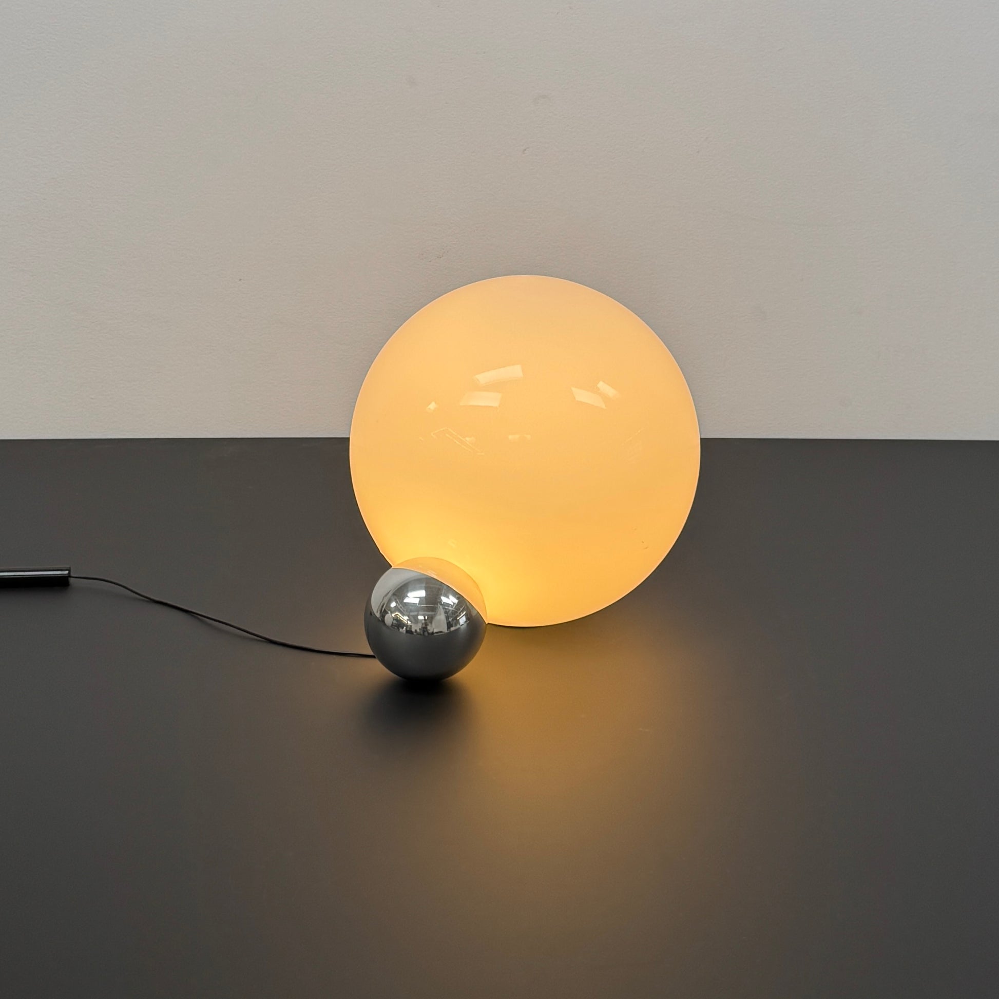 Two Flos Copycat Table Lamps by Flos, featuring glowing frosted glass spheres and chrome bases, make a sculptural statement on a dark surface against a light-colored wall.