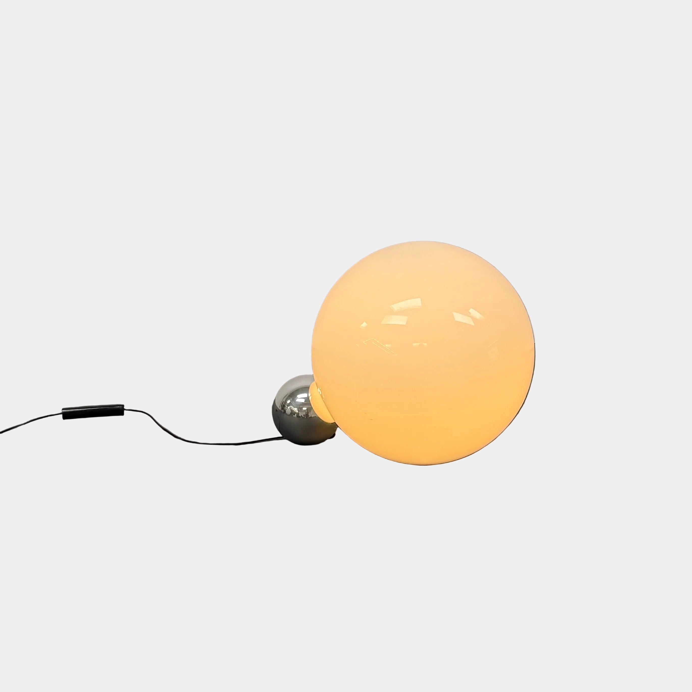 Two Flos Copycat Table Lamps by Flos, featuring glowing frosted glass spheres and chrome bases, make a sculptural statement on a dark surface against a light-colored wall.