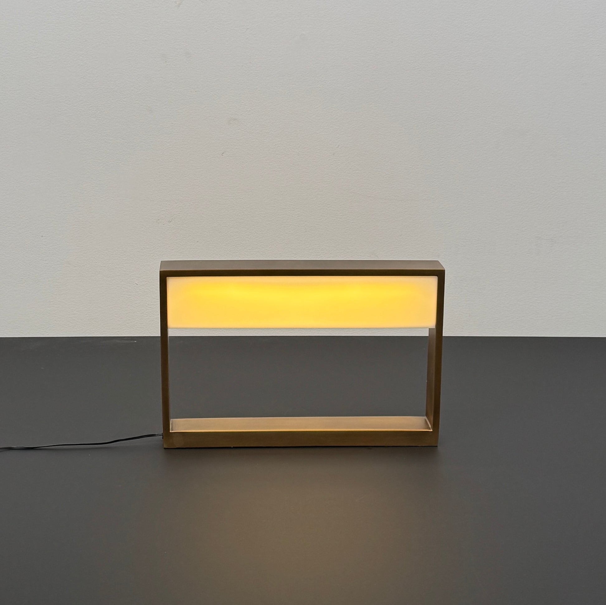 The Arterior Aura LED Table Lamp in Antique Brass by Arterior is paired with a modern console table featuring a gold rectangular frame and single white drawer, set against a plain white background.