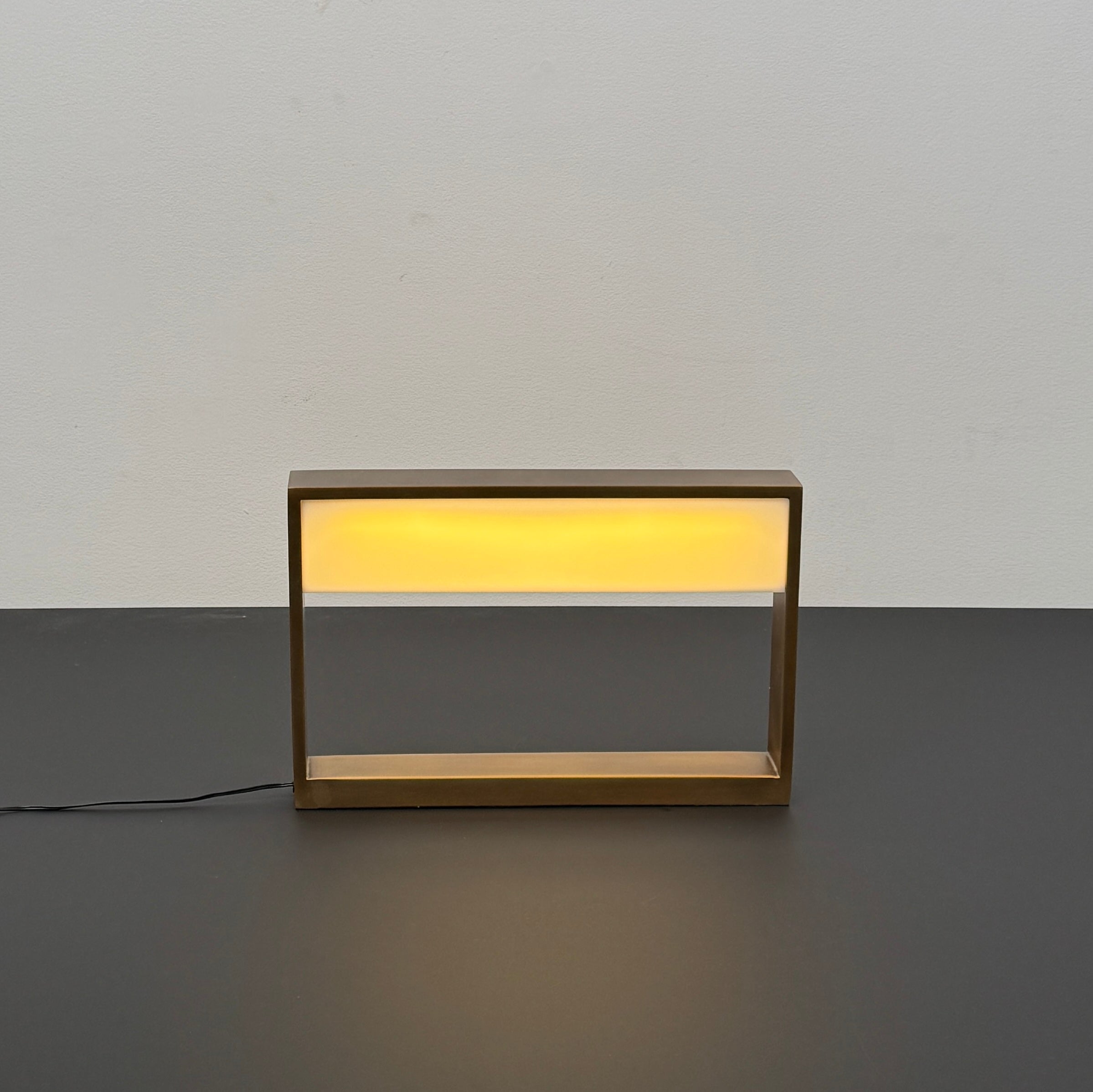 The Arterior Aura LED Table Lamp in Antique Brass by Arterior is paired with a modern console table featuring a gold rectangular frame and single white drawer, set against a plain white background.