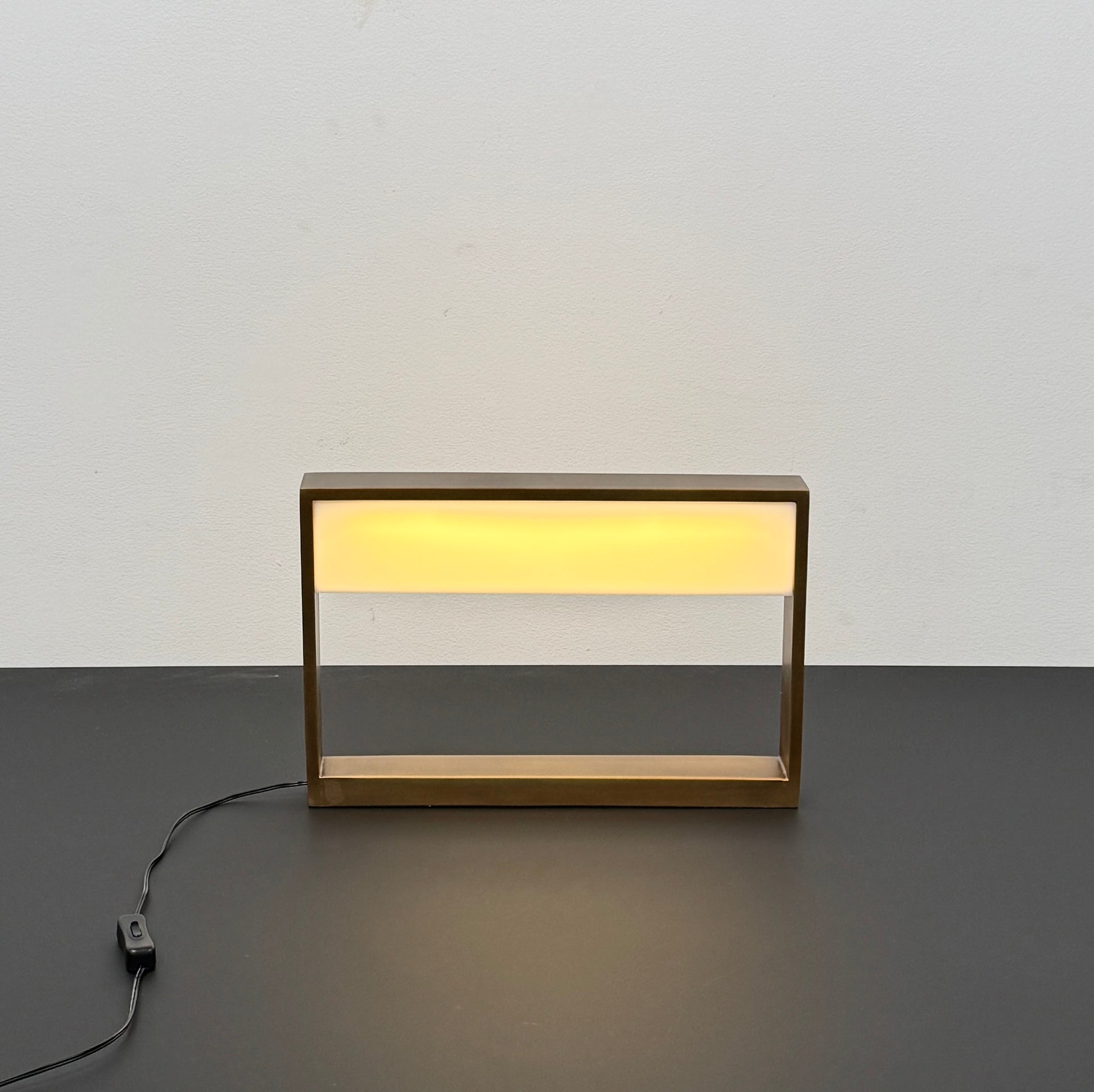 The Arterior Aura LED Table Lamp in Antique Brass by Arterior is paired with a modern console table featuring a gold rectangular frame and single white drawer, set against a plain white background.