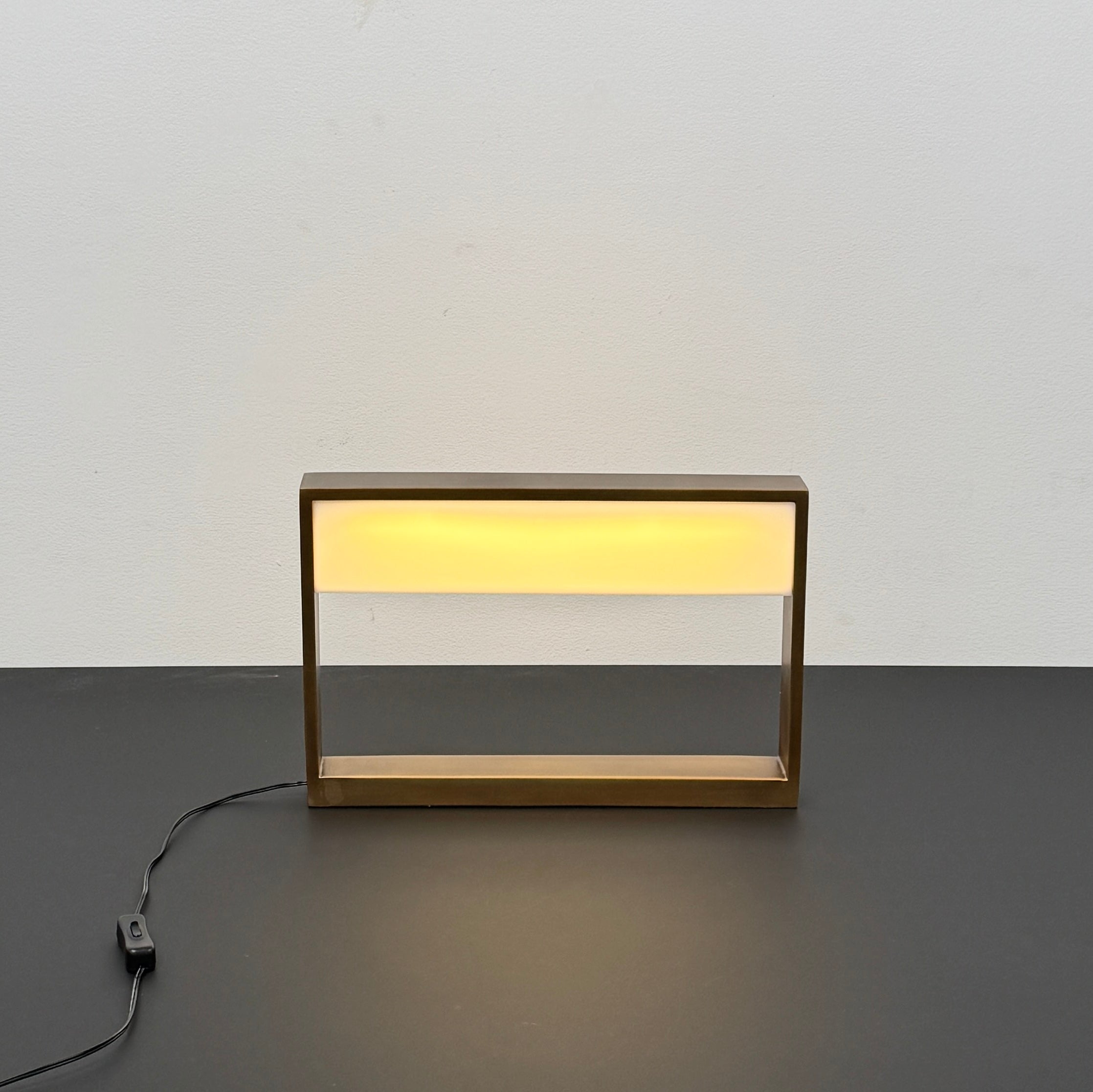 The Arterior Aura LED Table Lamp in Antique Brass by Arterior is paired with a modern console table featuring a gold rectangular frame and single white drawer, set against a plain white background.