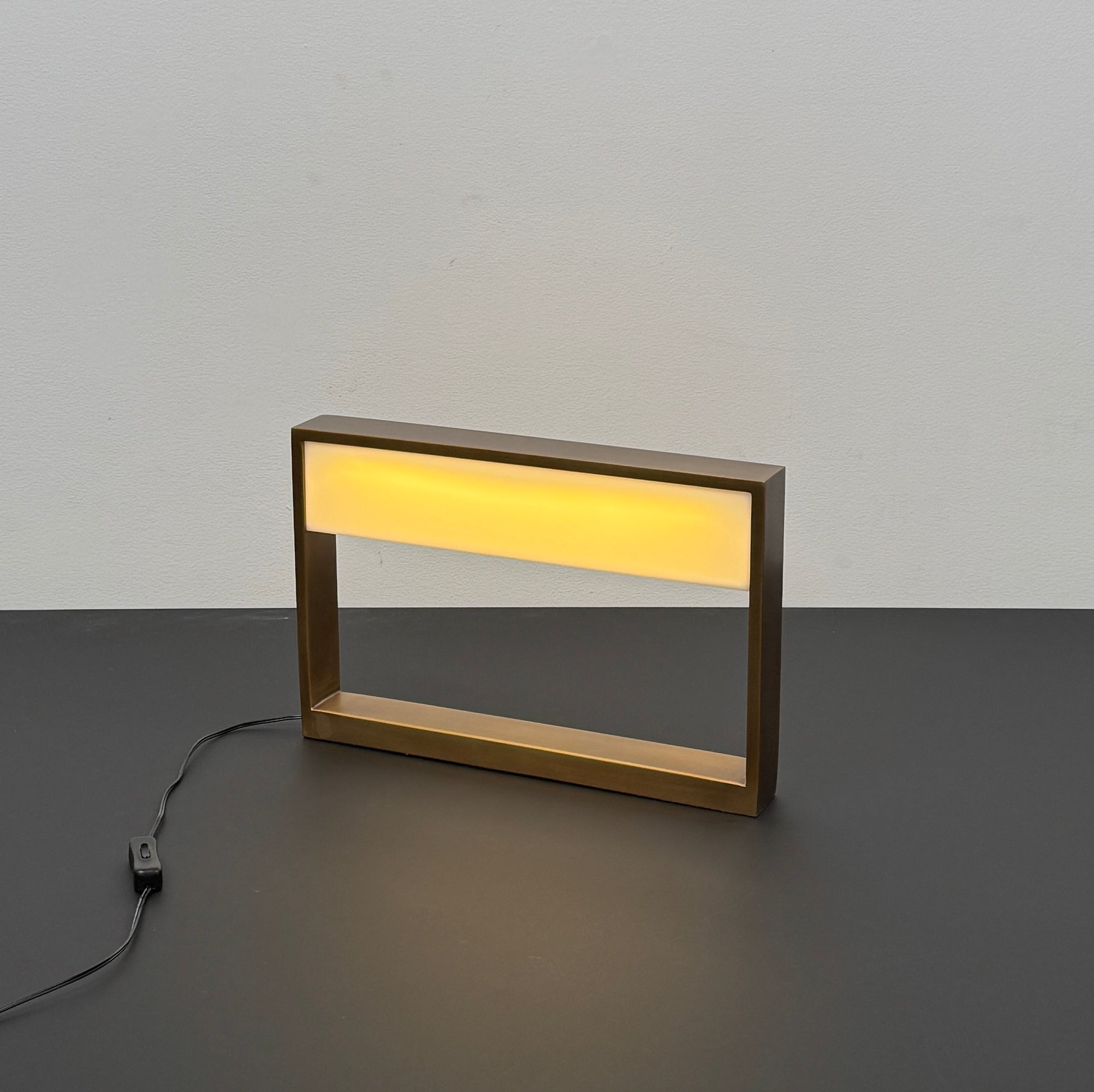 The Arterior Aura LED Table Lamp in Antique Brass by Arterior is paired with a modern console table featuring a gold rectangular frame and single white drawer, set against a plain white background.