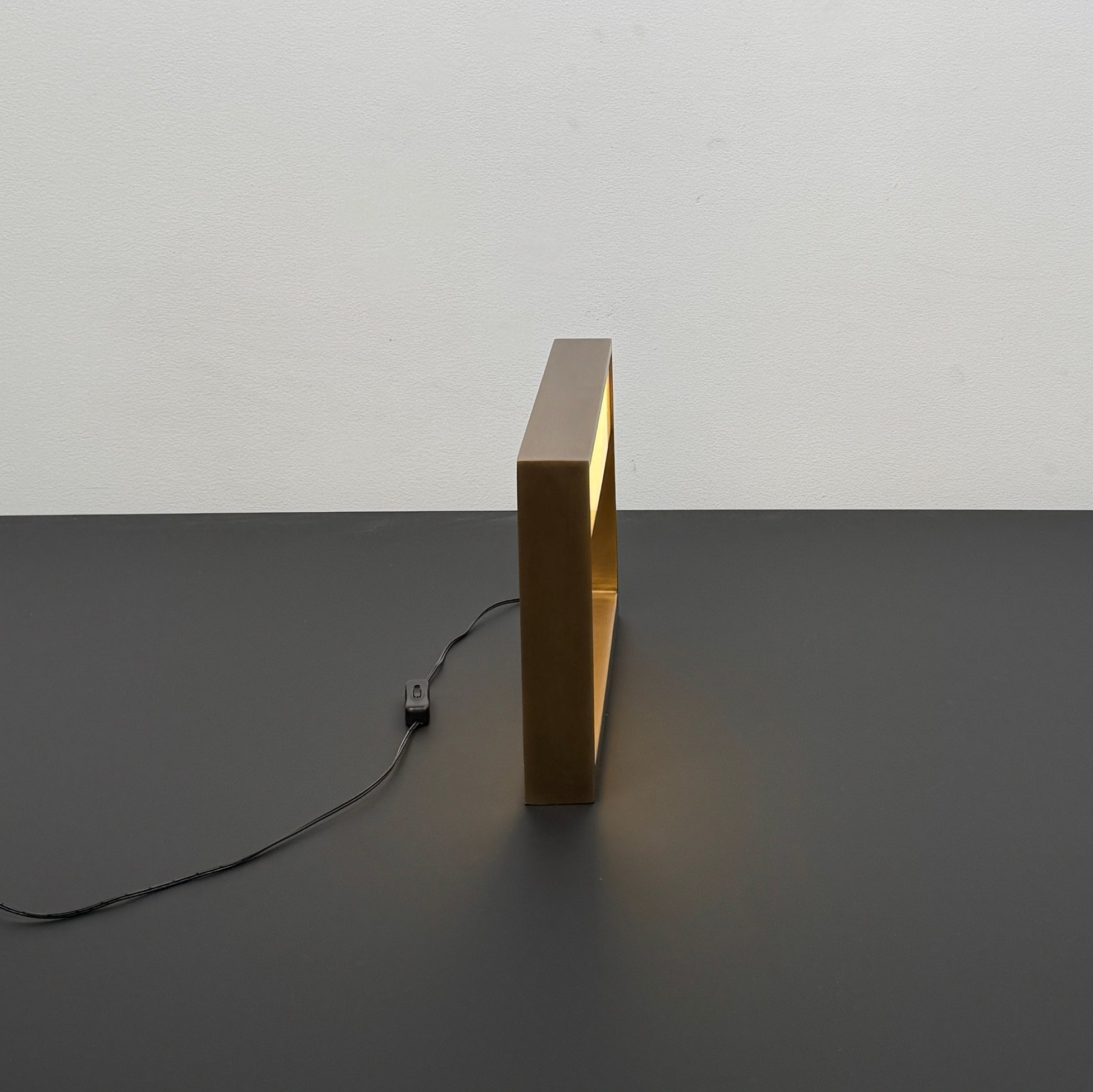 The Arterior Aura LED Table Lamp in Antique Brass by Arterior is paired with a modern console table featuring a gold rectangular frame and single white drawer, set against a plain white background.