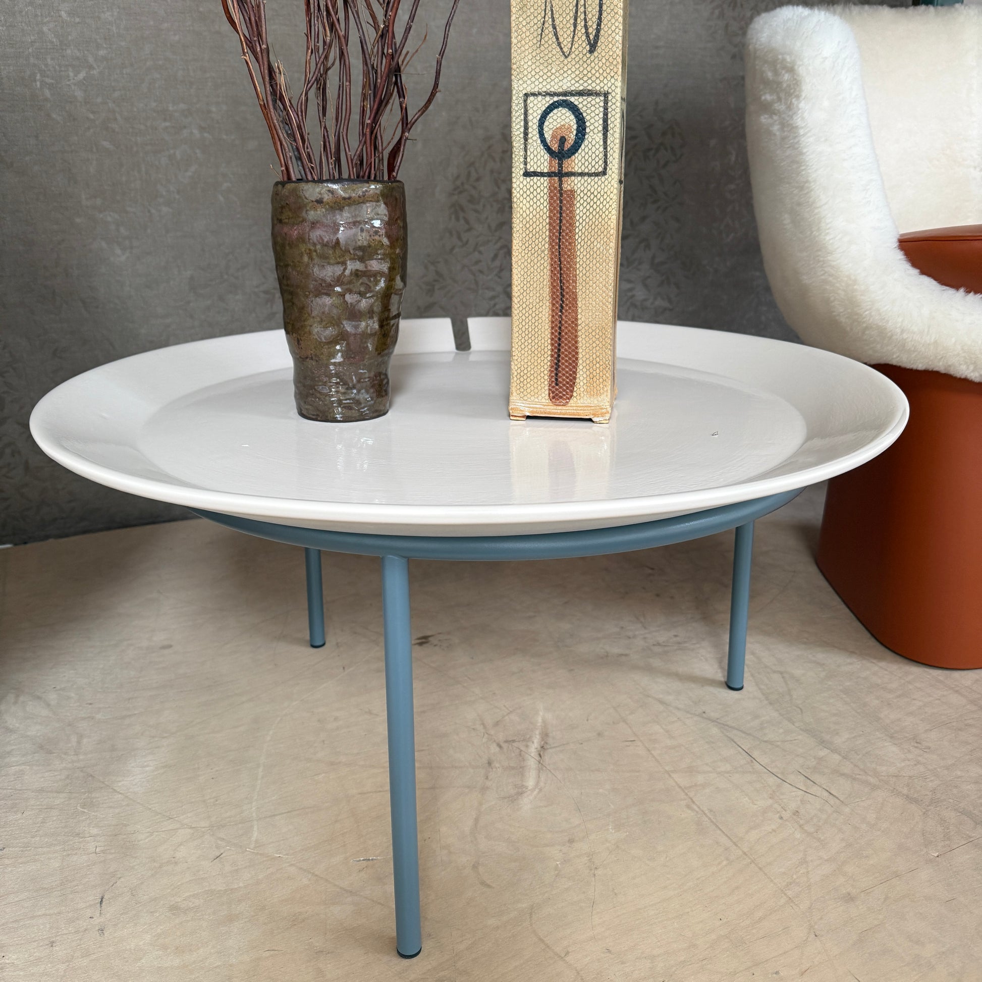 The Gervasoni Brise 54 Outdoor Coffee Table by Gervasoni features a round beige tray top and three black metal legs, shown against a light grey background—perfect for adding modern style to outdoor spaces.