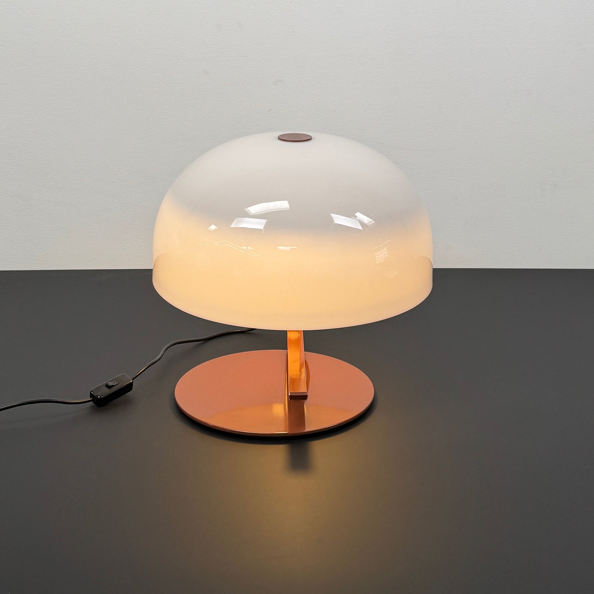 The Oluce Zanuso 275 Table Light by Oluce is a modern lamp inspired by Italian design, with a white domed glass shade, orange base, and black power cord with switch, shown against a plain background.