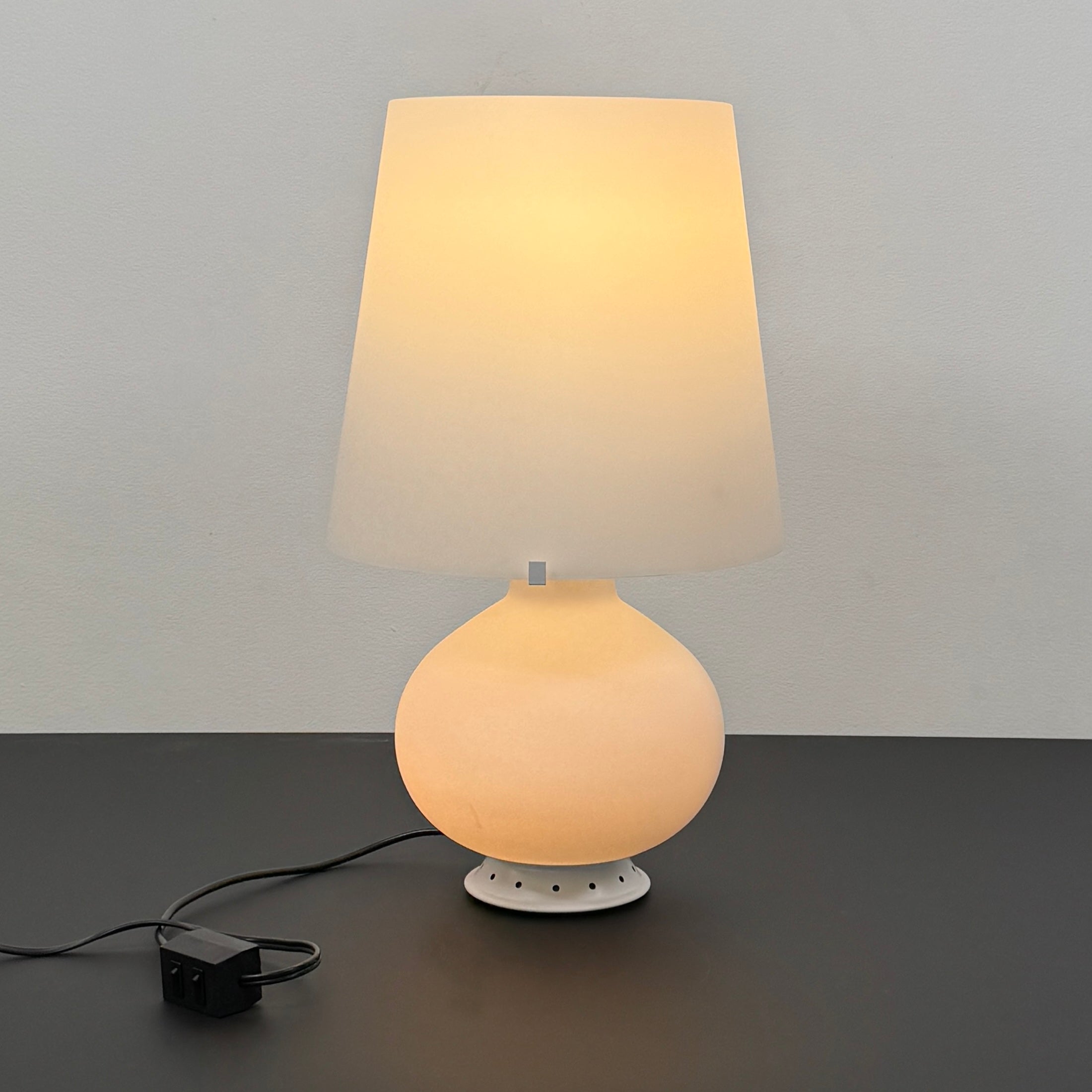 The Fontana Arte Table Lamp - Medium by Fontana Arte features a modernist design with a round base and wide, tapered lampshade, displayed against a plain light background.