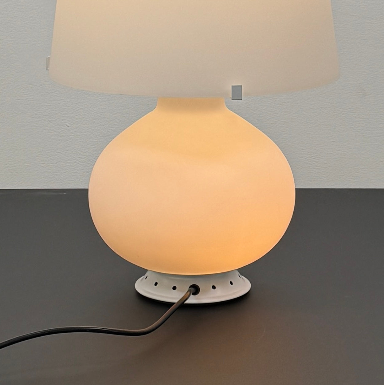 The Fontana Arte Table Lamp - Medium by Fontana Arte features a modernist design with a round base and wide, tapered lampshade, displayed against a plain light background.