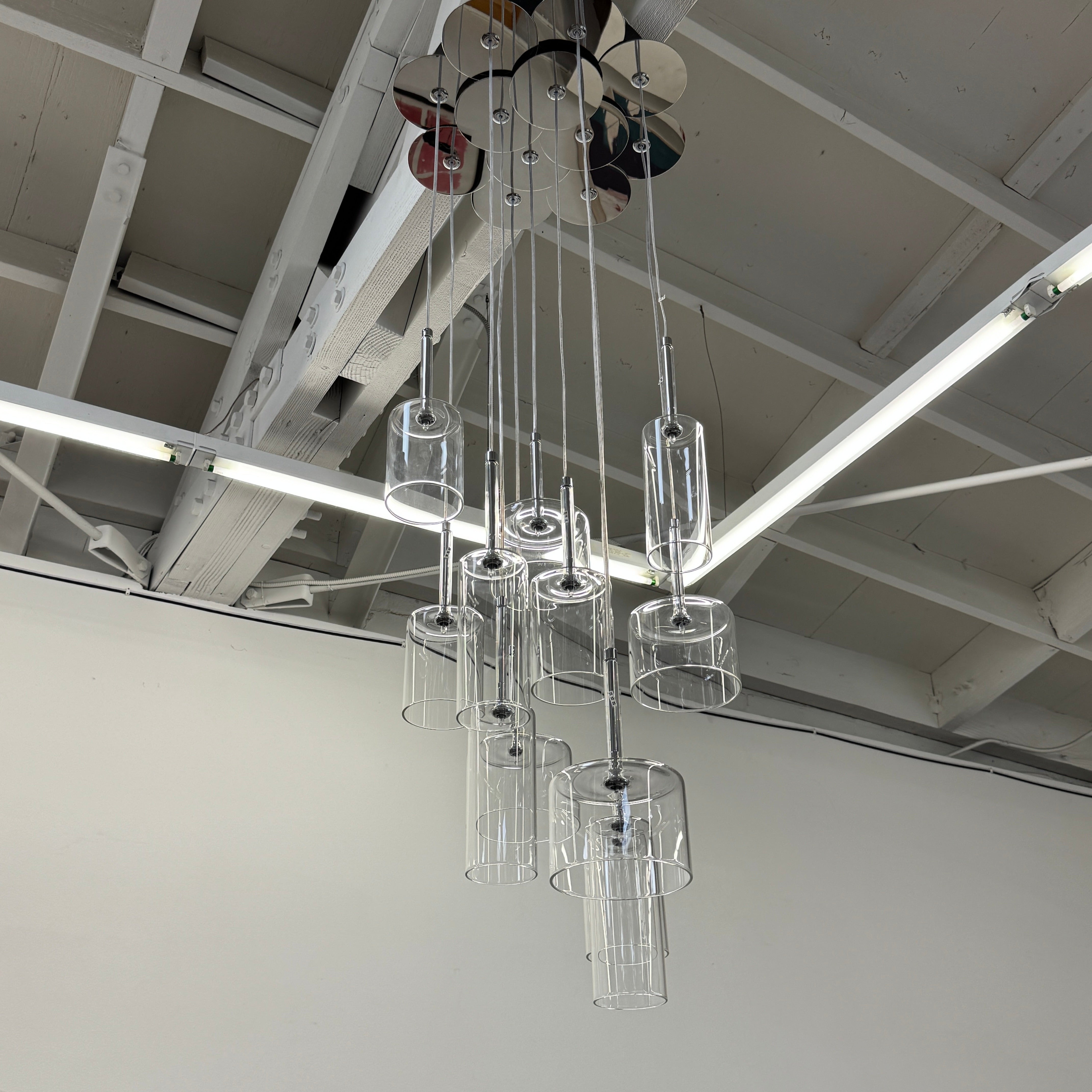 The AXO Light Axolight 12 Light Spillray Suspension Light features modern cylindrical glass pendants on black cords from a round ceiling mount, ideal for contemporary lighting schemes.