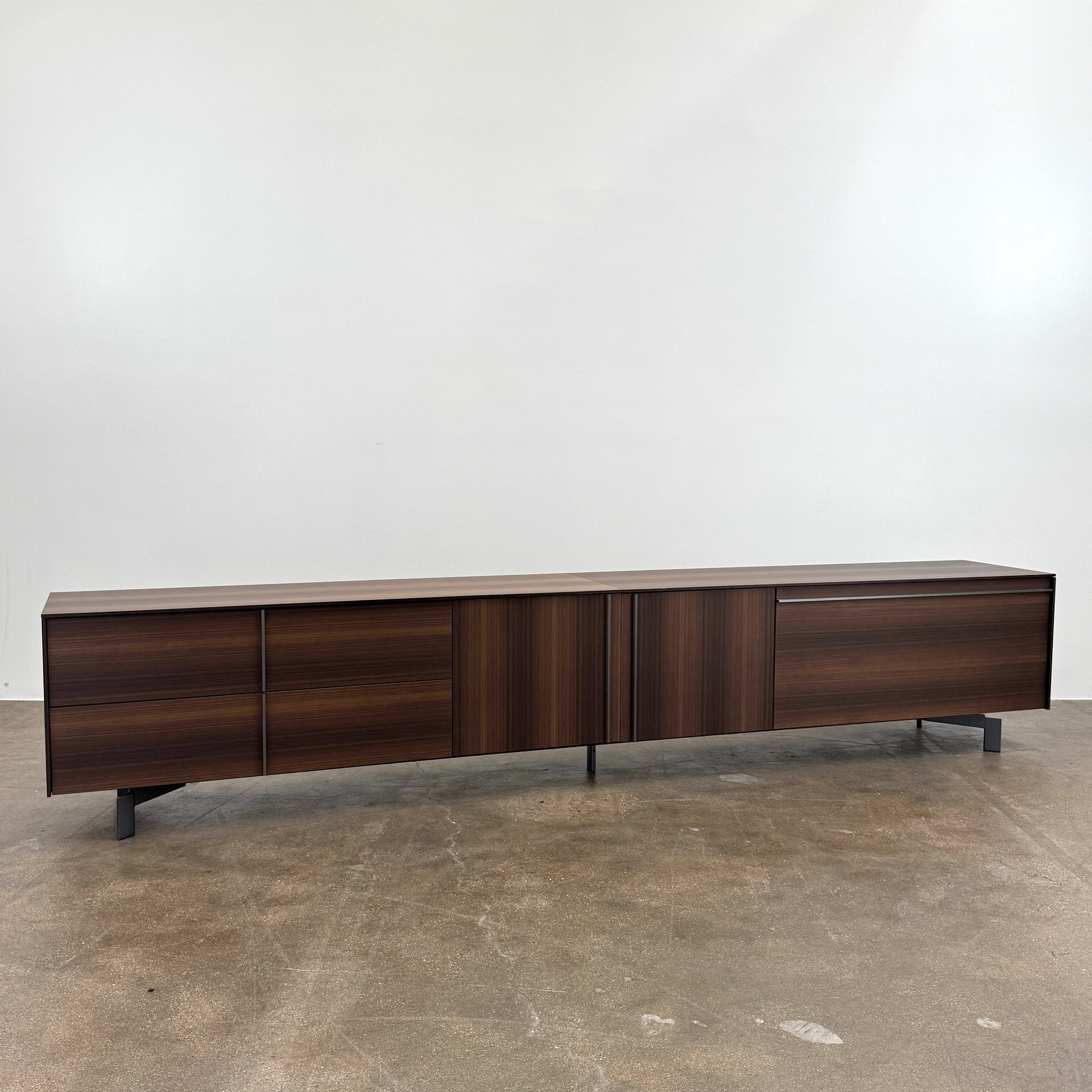 The Molteni & C Pass-word Console by Molteni & C is a modern, low-profile Eucalyptus wood sideboard with two drawers, cabinets on each side, and black metal legs, shown against a plain white background.