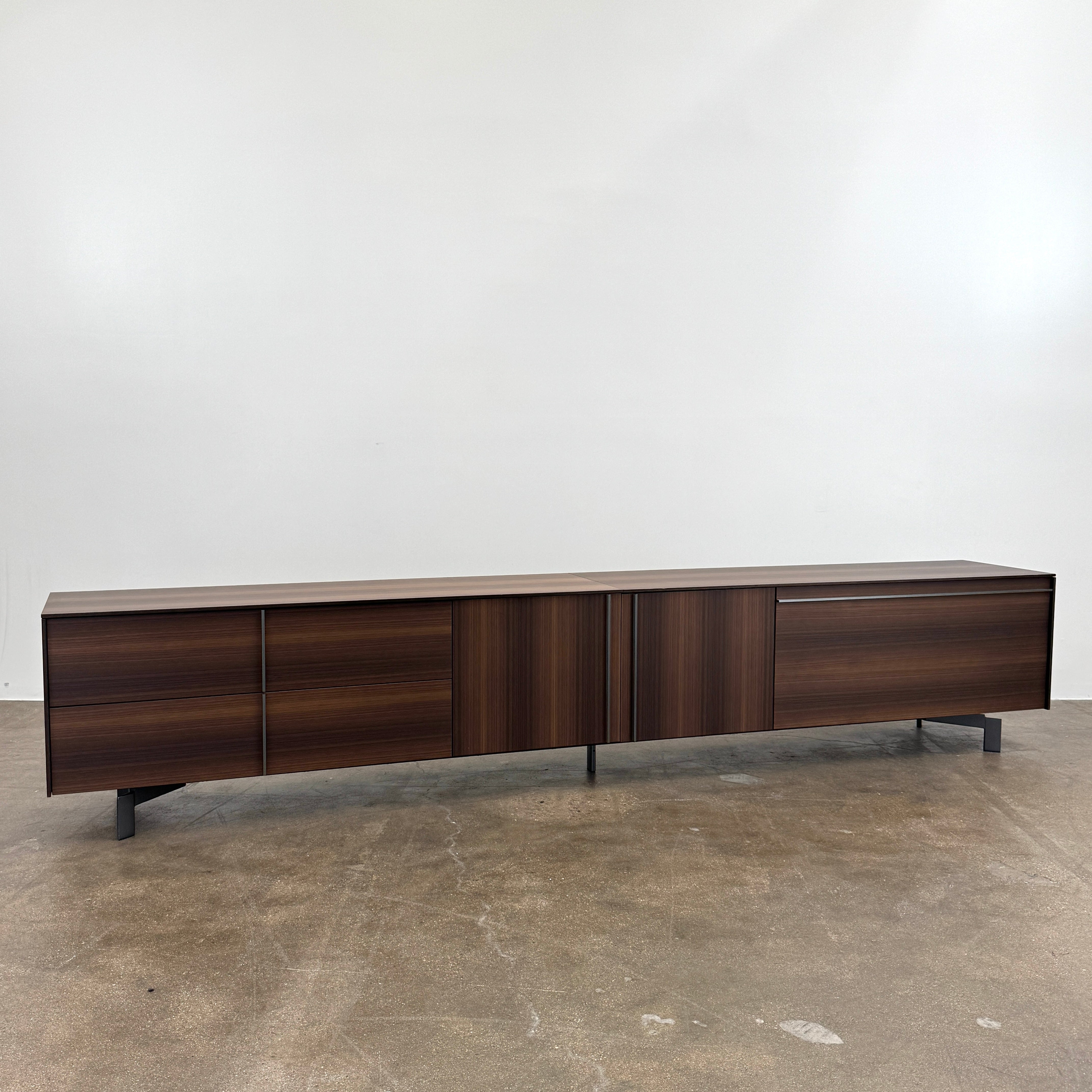 The Molteni & C Pass-word Console by Molteni & C is a modern, low-profile Eucalyptus wood sideboard with two drawers, cabinets on each side, and black metal legs, shown against a plain white background.