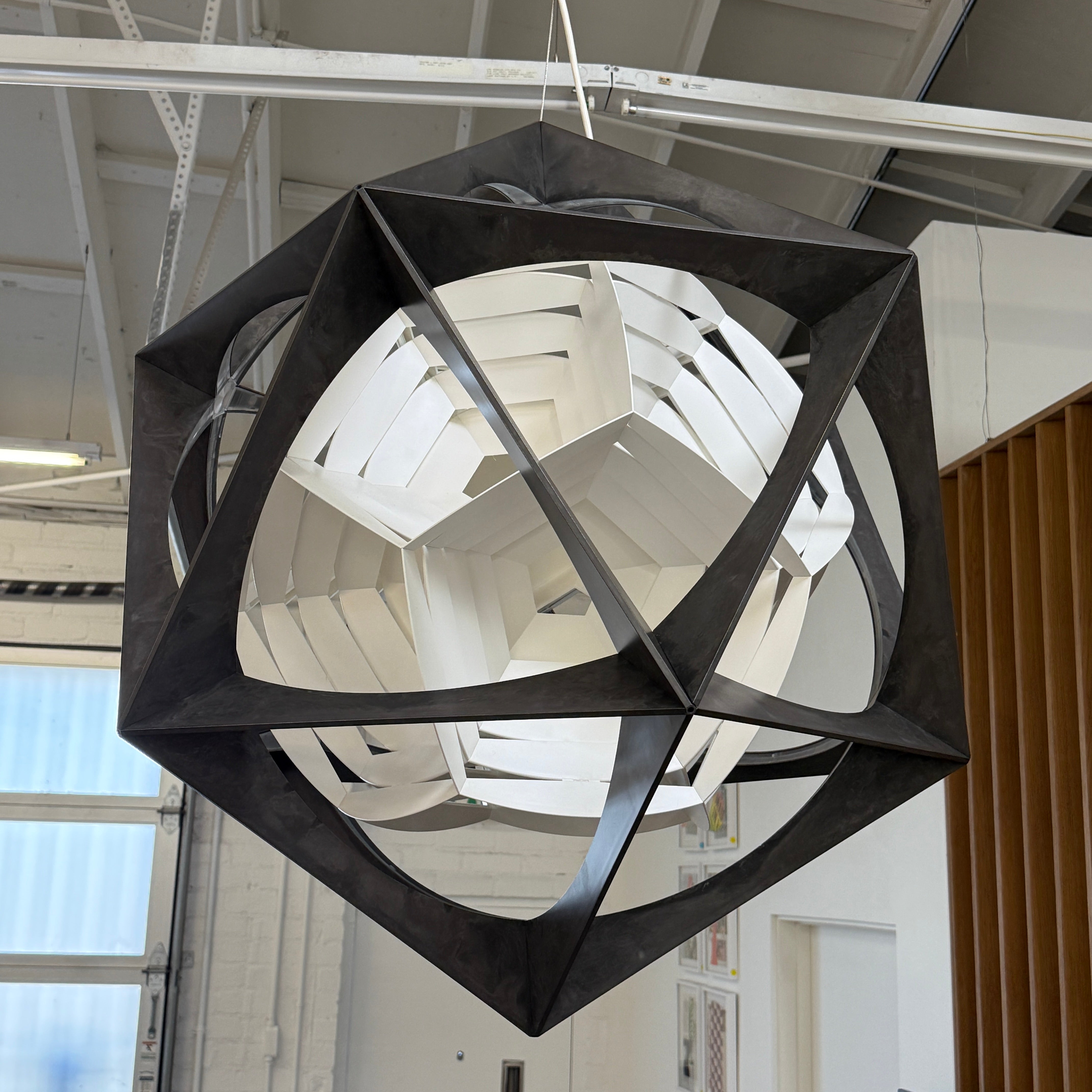 The Louis Poulsen OE Quasi Pendant is a sculptural geometric light fixture featuring a black outer frame and layered white panels, elegantly suspended by a cord—a modern design by Louis Poulsen.