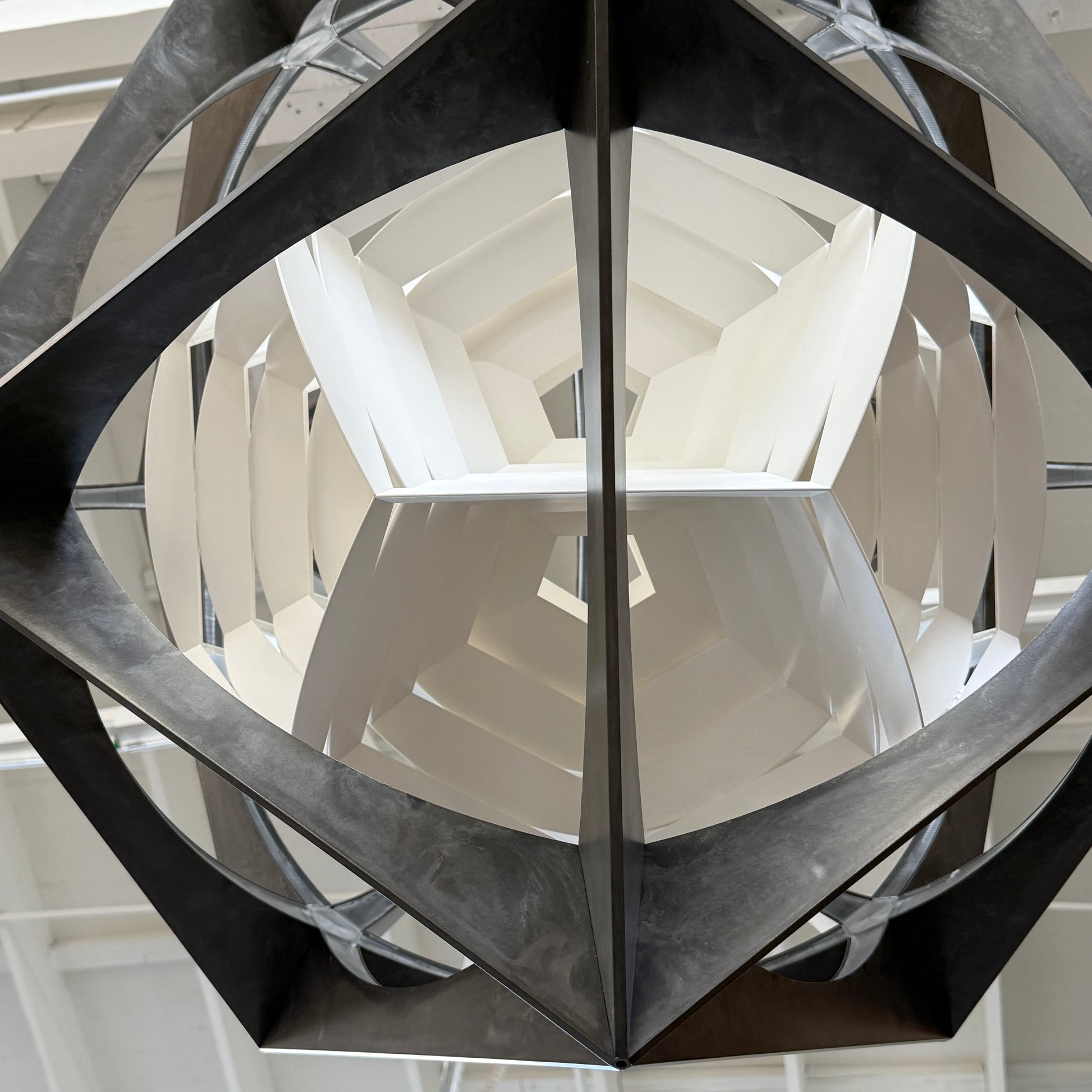 The Louis Poulsen OE Quasi Pendant is a sculptural geometric light fixture featuring a black outer frame and layered white panels, elegantly suspended by a cord—a modern design by Louis Poulsen.