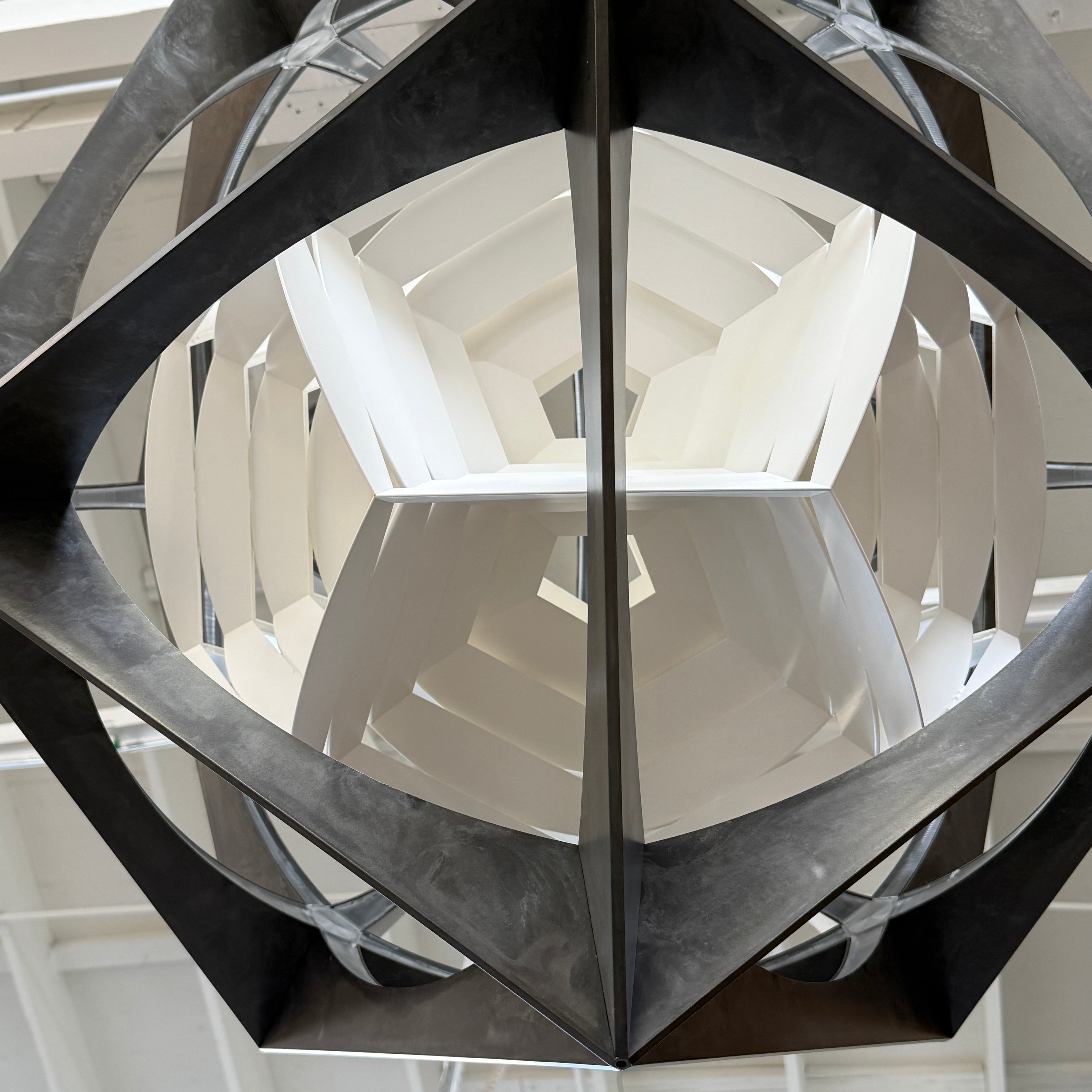 The Louis Poulsen OE Quasi Pendant is a sculptural geometric light fixture featuring a black outer frame and layered white panels, elegantly suspended by a cord—a modern design by Louis Poulsen.